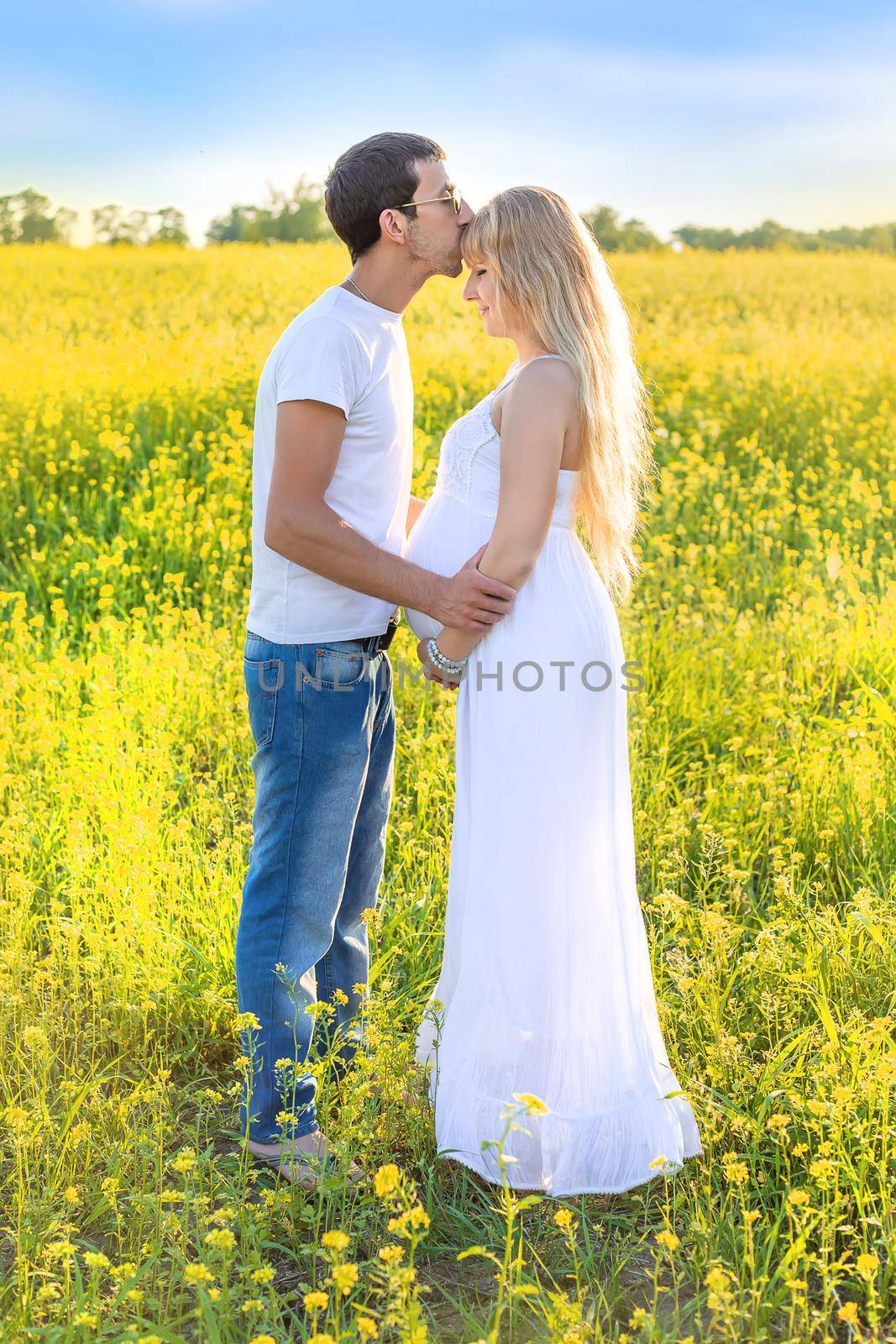 Pregnant woman and man photo shoot in mustard field. Selective focus.