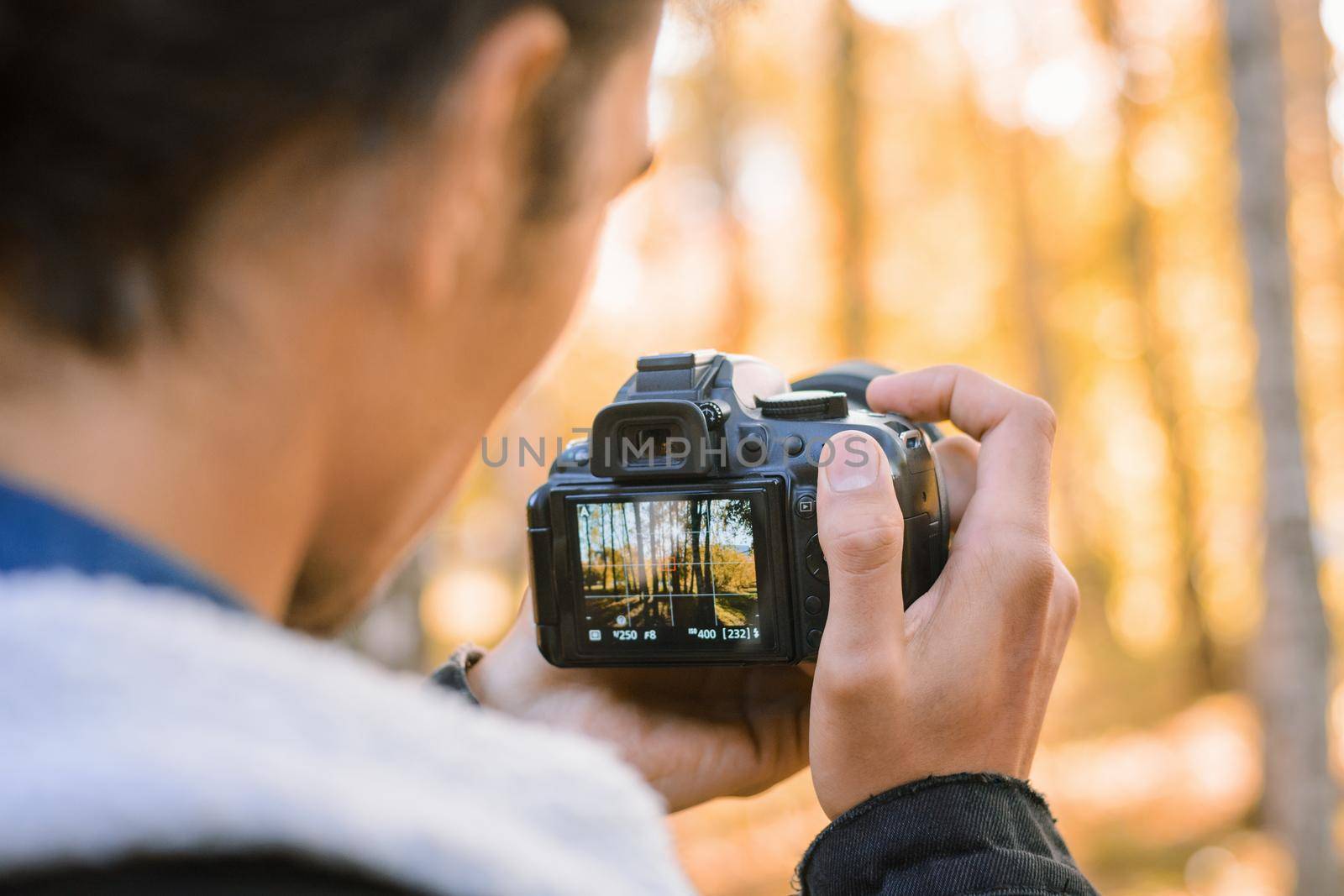Passionate nature photographer shooting photos and videos in autumn forest, using his modern professional camera to catch beautiful moments of fall