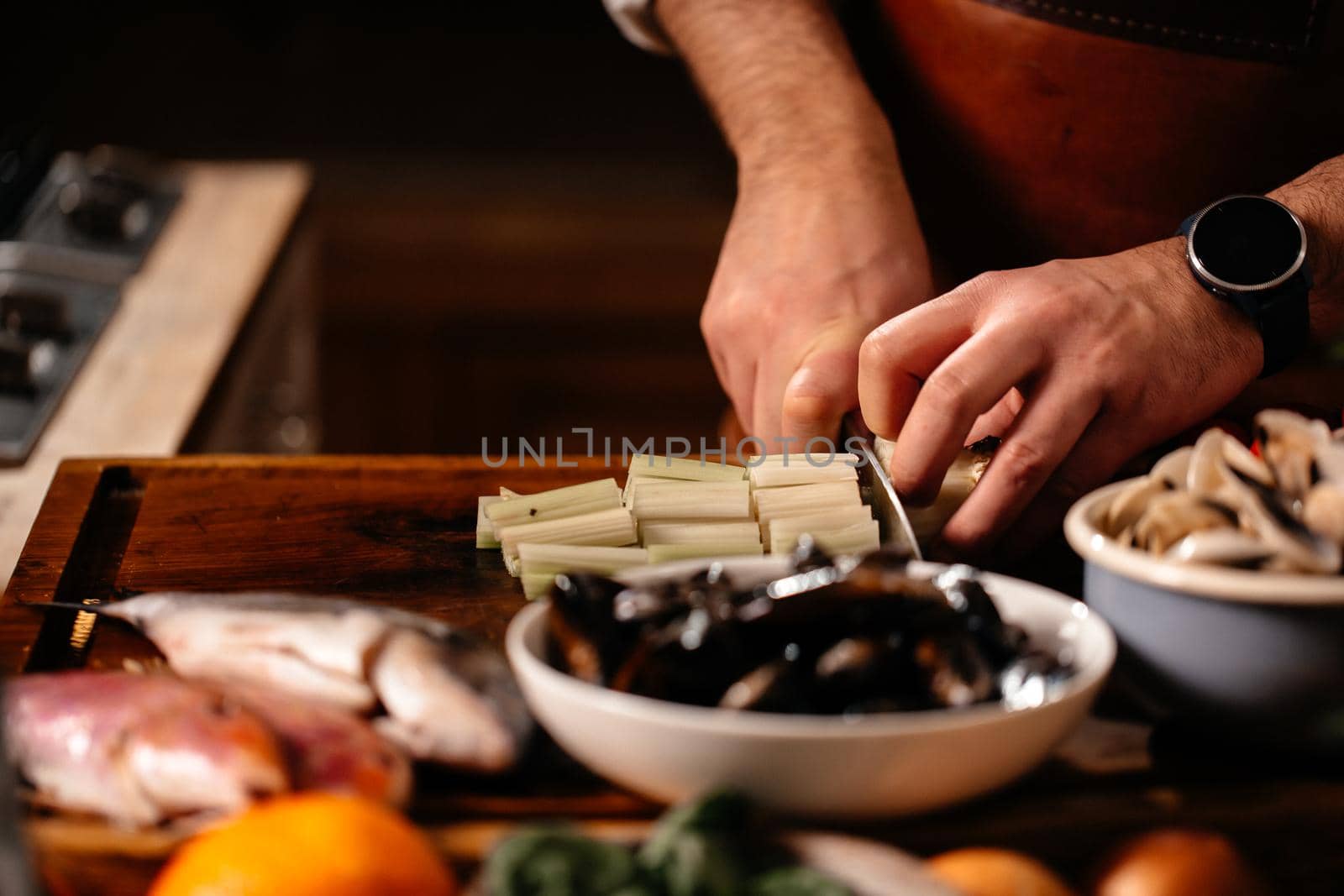 Cook chopping celery on cutting board surrounded by a variety of ingredients. Fresh Mollusks Fish Shell Shrimp. Cooking Seafood.