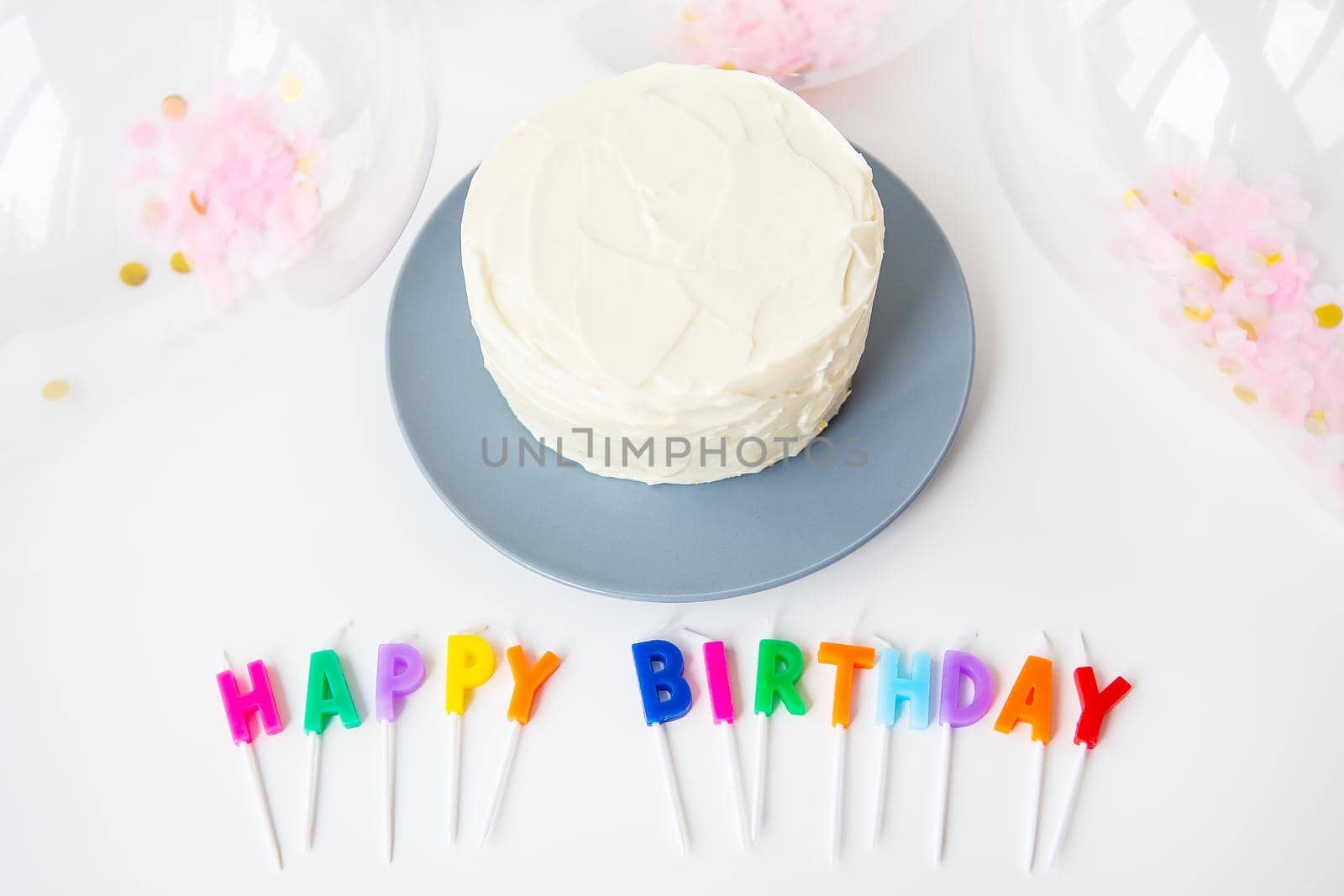 Colorful candles with Happy Birthday lettering isolated on white background along with confetti and bento cake. Holiday and surprise concept