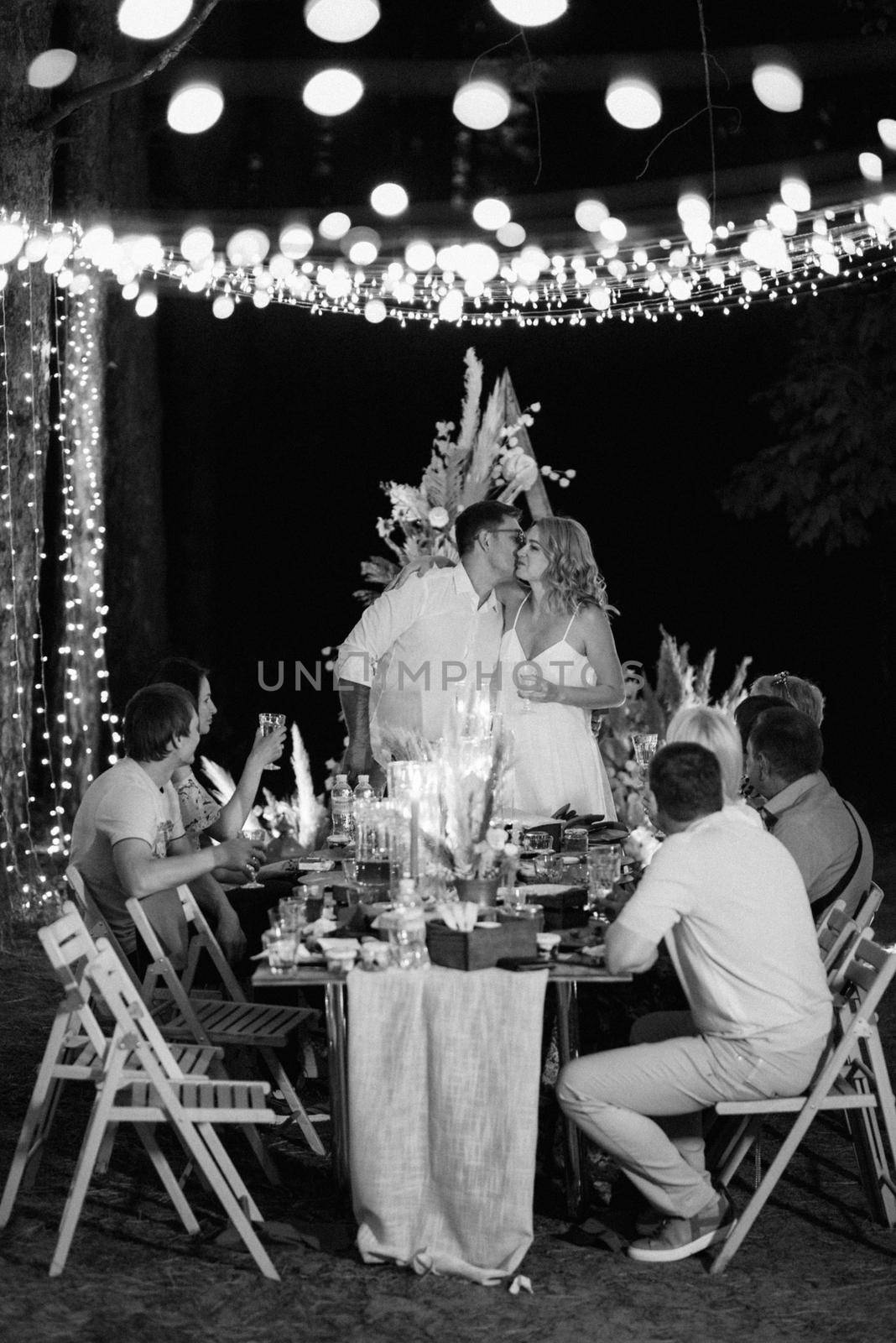 evening wedding family dinner in the forest with light bulbs and candles