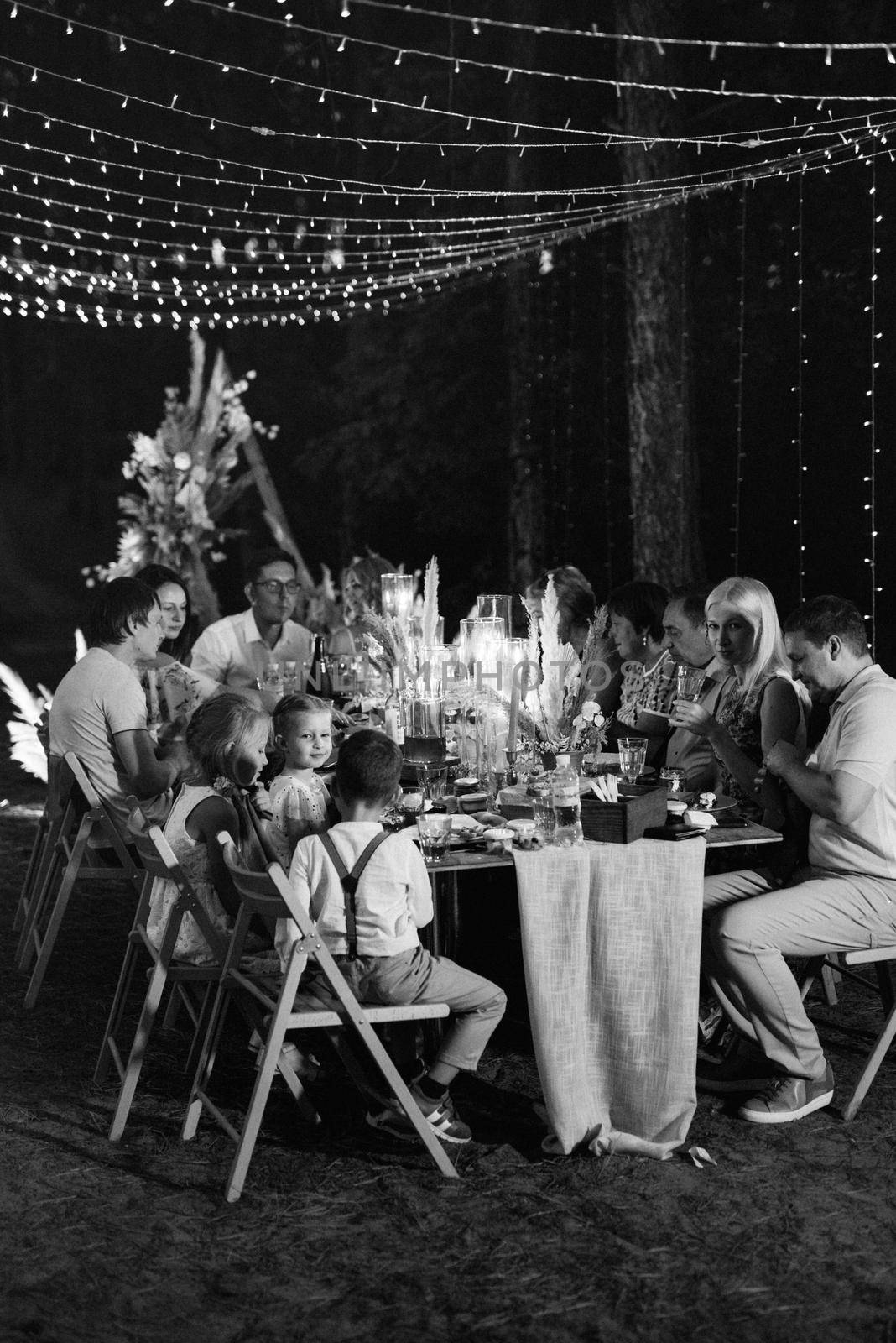 evening wedding family dinner in the forest with light bulbs and candles