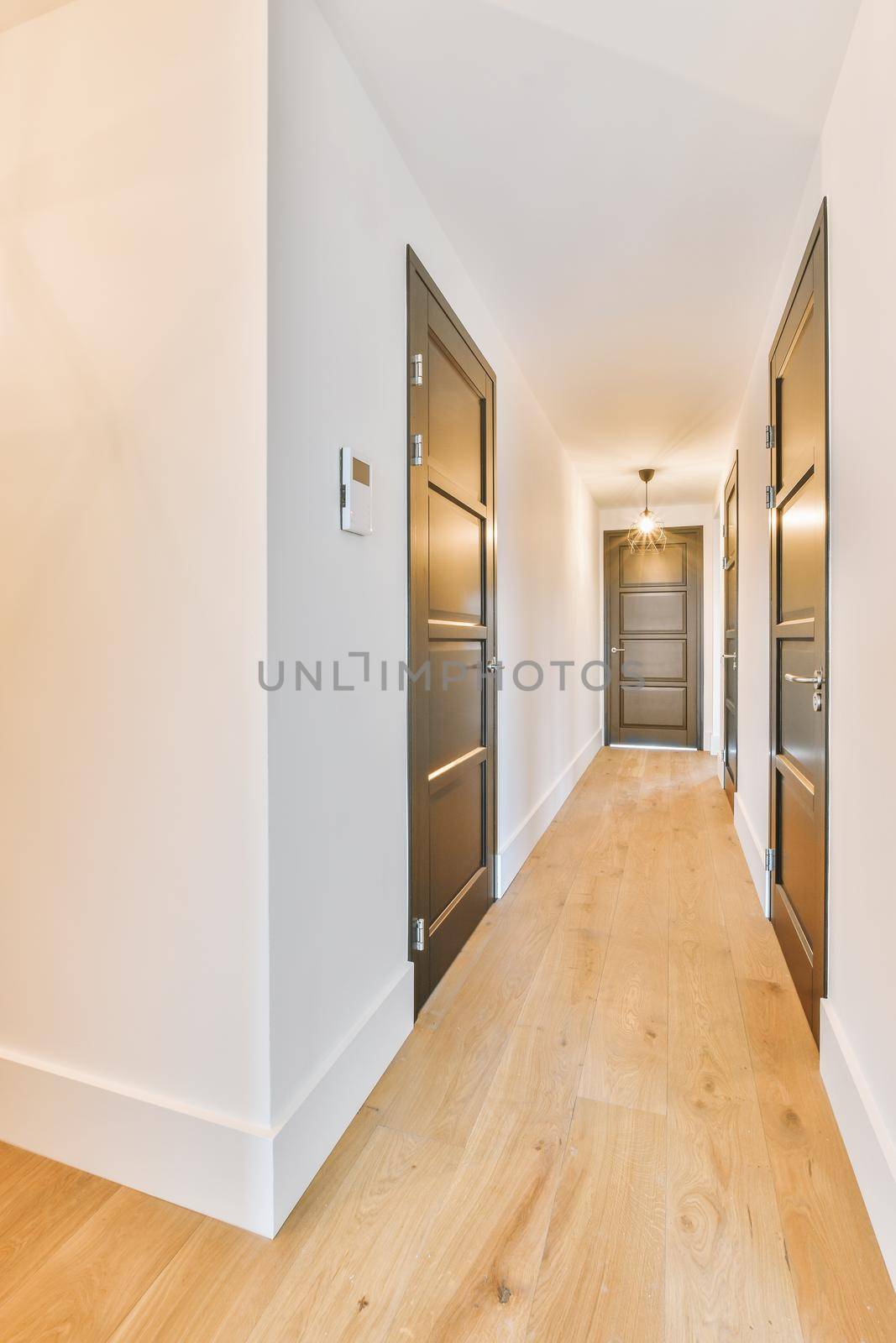 Light narrow hallway with many doors in white walls and glowing lamp over lumber floor