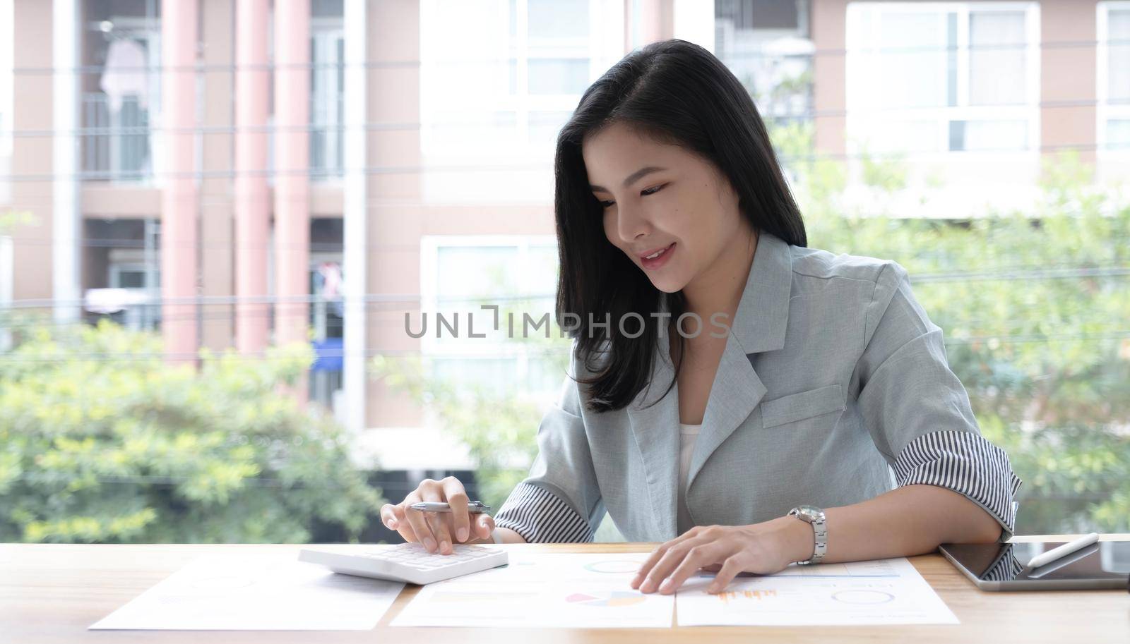 Business woman using calculator and writing make note with calculate. Woman working at office with laptop and documents on his desk by wichayada