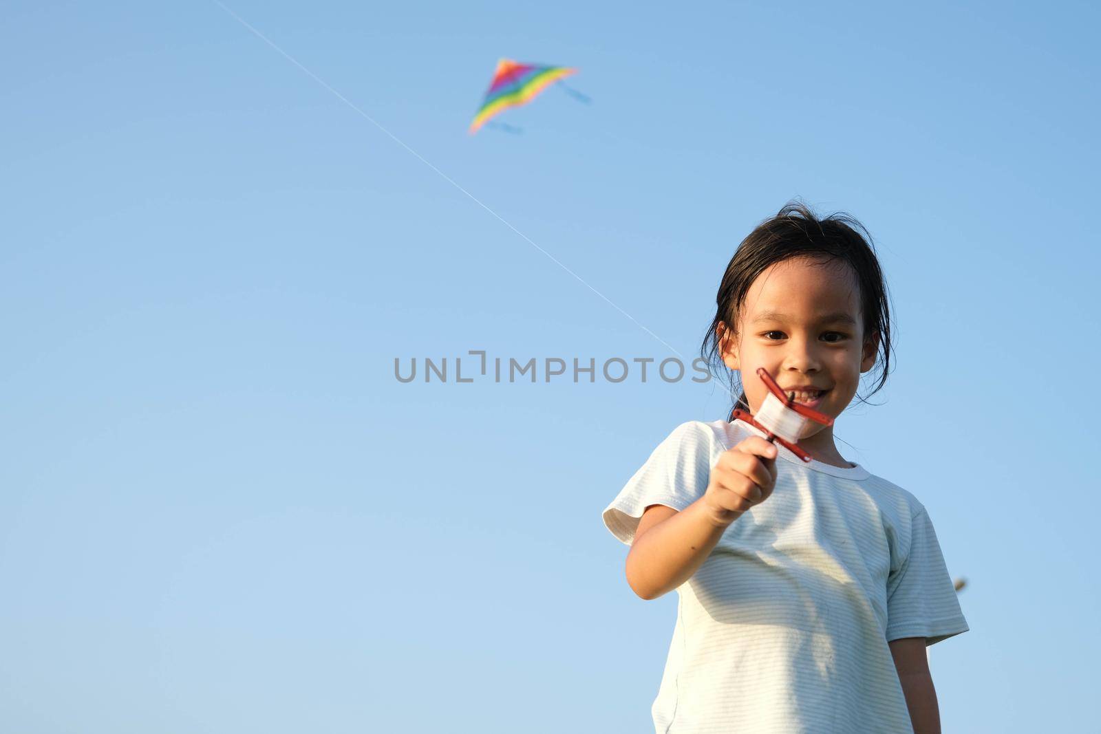 Child playing with a kite while running on a meadow by the lake at sunset. Healthy summer activity for children. Funny time with family. by TEERASAK