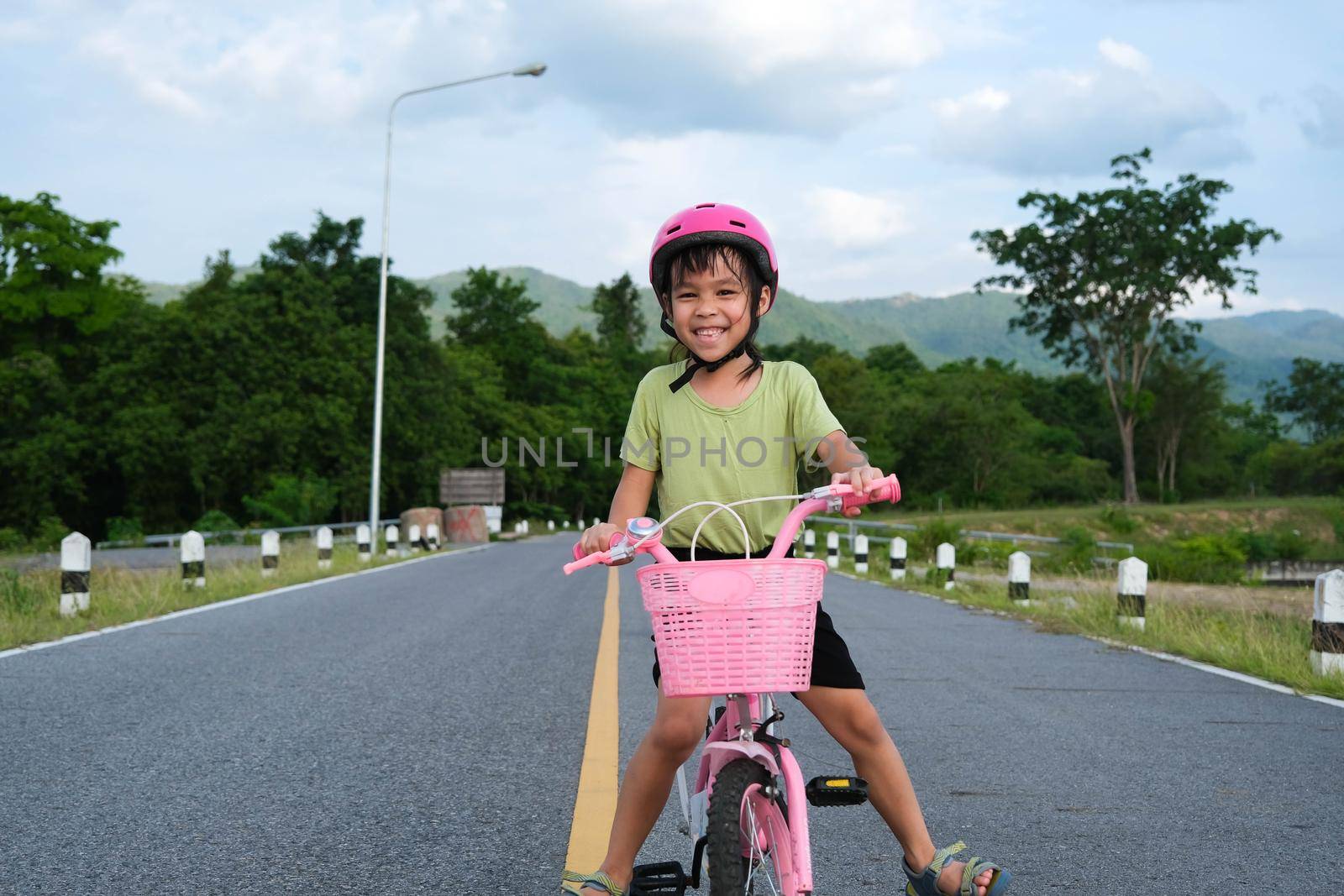 Cute little girl in a helmet riding a bicycle on an asphalt road in summer. Happy little girl riding a bicycle outdoors. Healthy Summer Activities for Kids