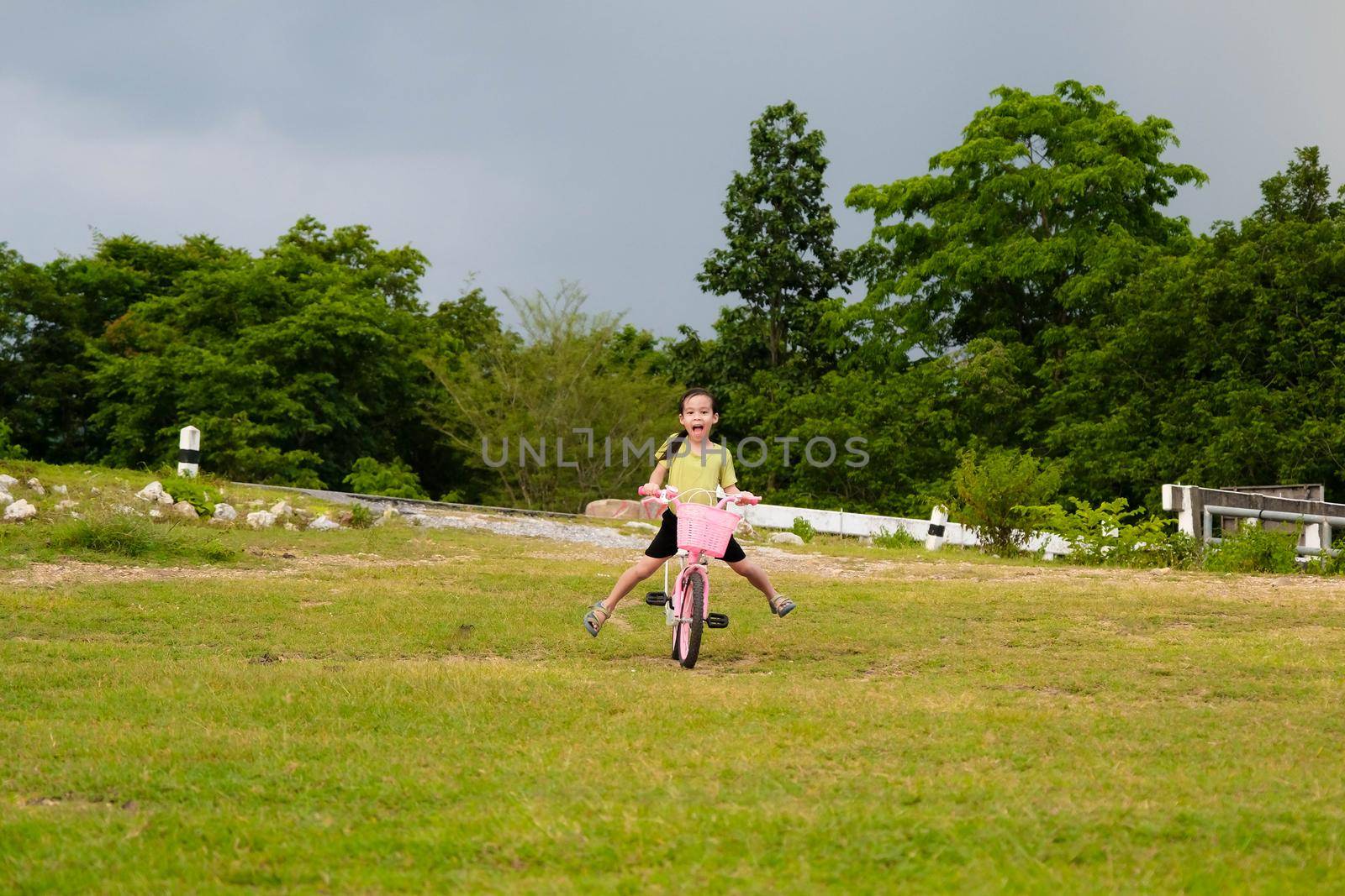 Cute Asian little girl riding a bicycle on the lawn on a hot summer day. Happy little girl riding a bicycle outdoors. Healthy Summer Activities for Kids by TEERASAK