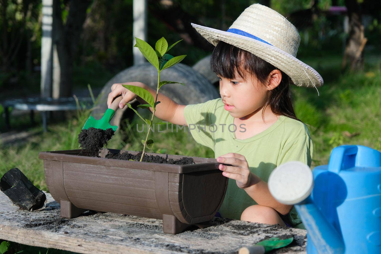 Little girl wearing a hat helps her mother in the garden, a little gardener. Cute girl planting flowers in pots for sale. family small business by TEERASAK