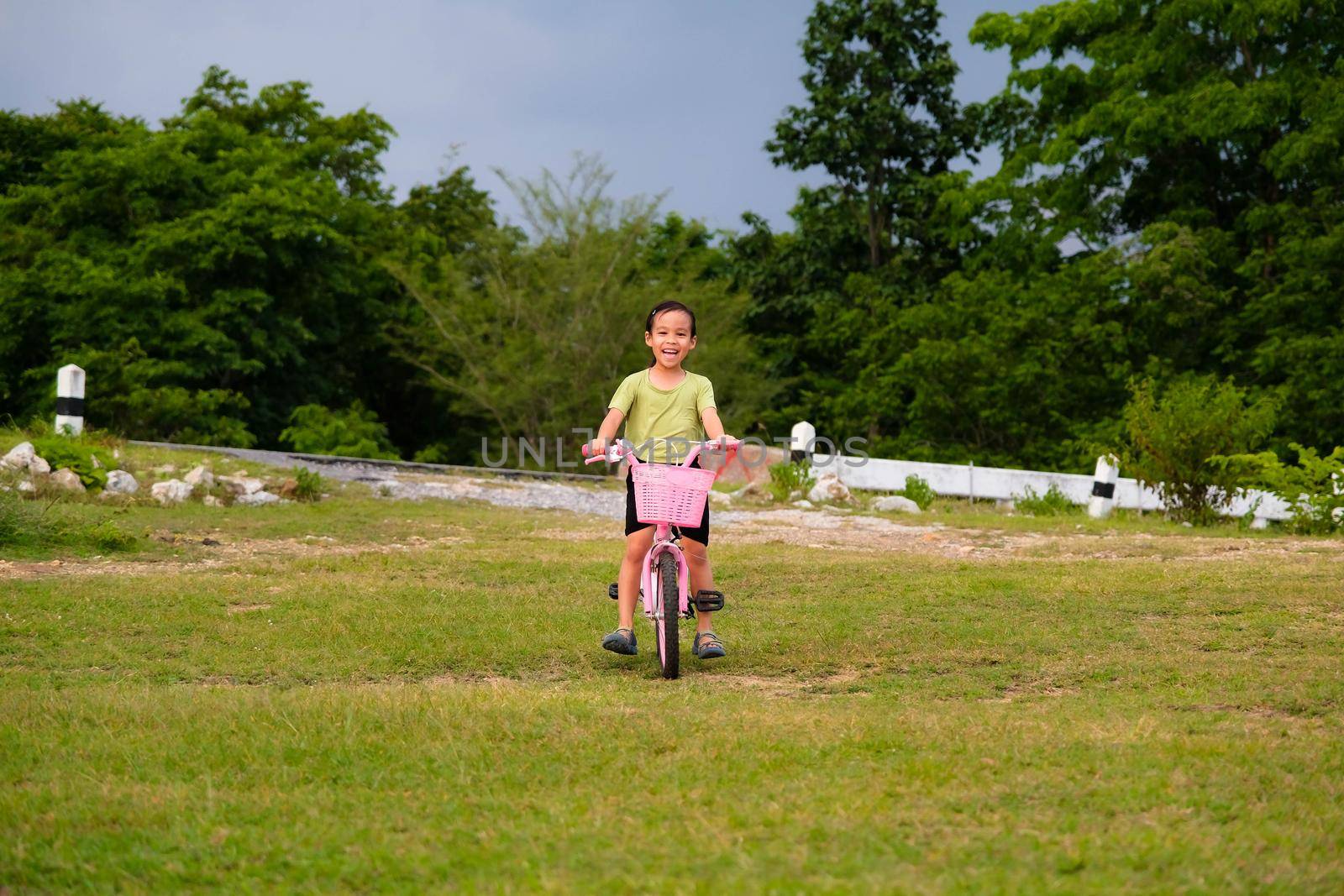 Cute Asian little girl riding a bicycle on the lawn on a hot summer day. Happy little girl riding a bicycle outdoors. Healthy Summer Activities for Kids