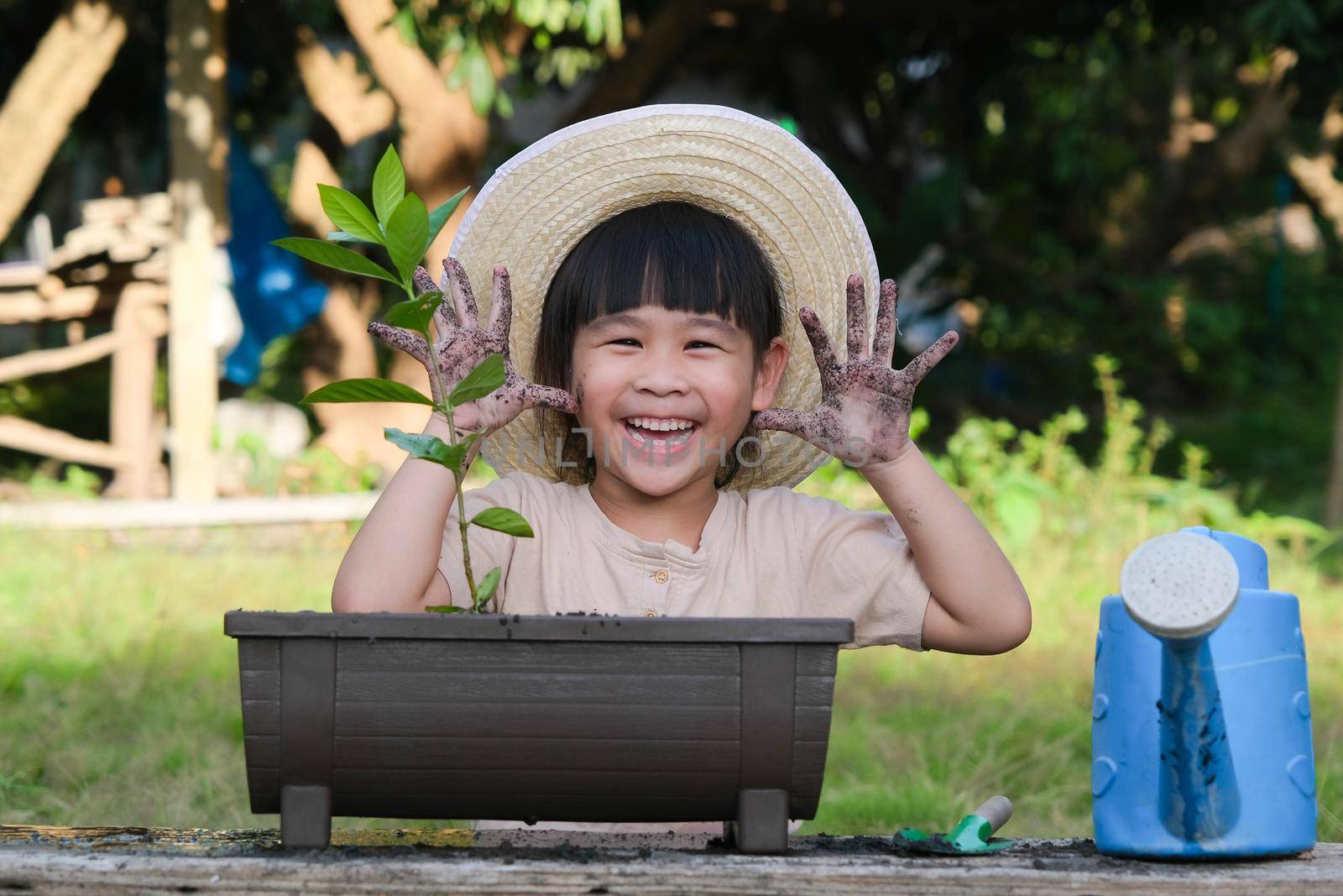 Little girl wearing a hat helps her mother in the garden, a little gardener. Cute girl planting flowers in pots. Cute little girl smiles and shows off her dirty hands in the backyard. by TEERASAK