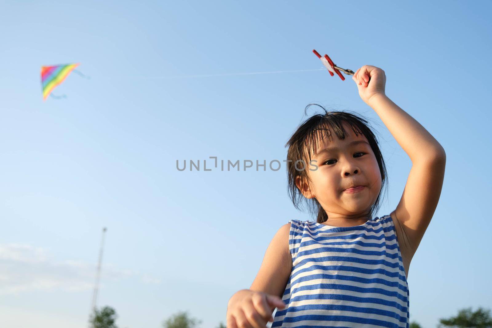 Child playing with a kite while running on a meadow by the lake at sunset. Healthy summer activity for children. Funny time with family.