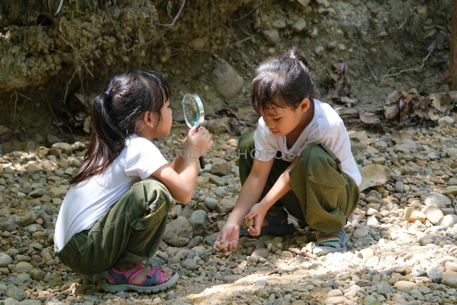Asian tourist family, two sisters studying rocks with a magnifying glass as they travel to Pha Chor is high soil canyon cliffs at Mae Wang National parks in Chiang Mai,Thailand. by TEERASAK