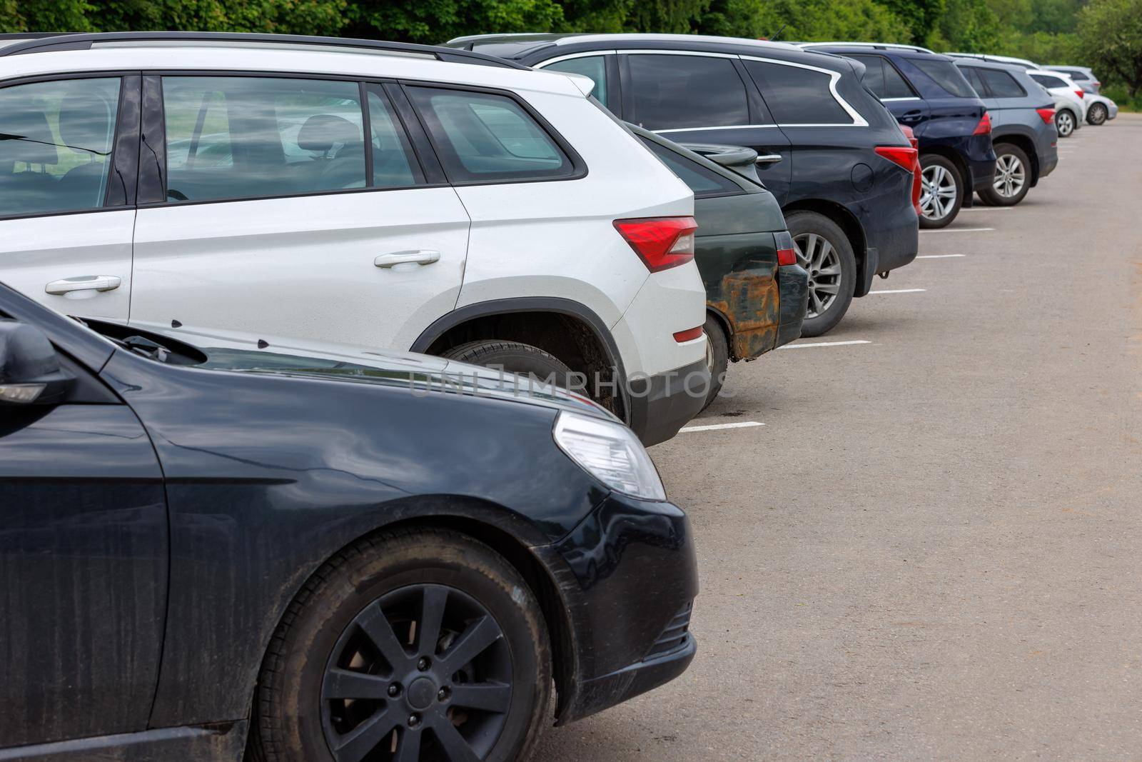 row of different color cars on asphalt parking lot at cloudy summer day with selective focus