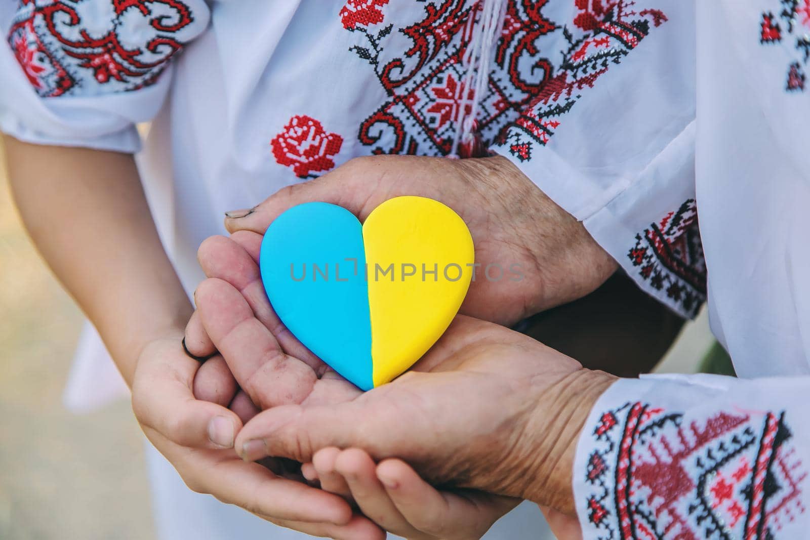 Grandmother holds in her hands a heart in the color of the Ukrainian flag. Selective focus. People.