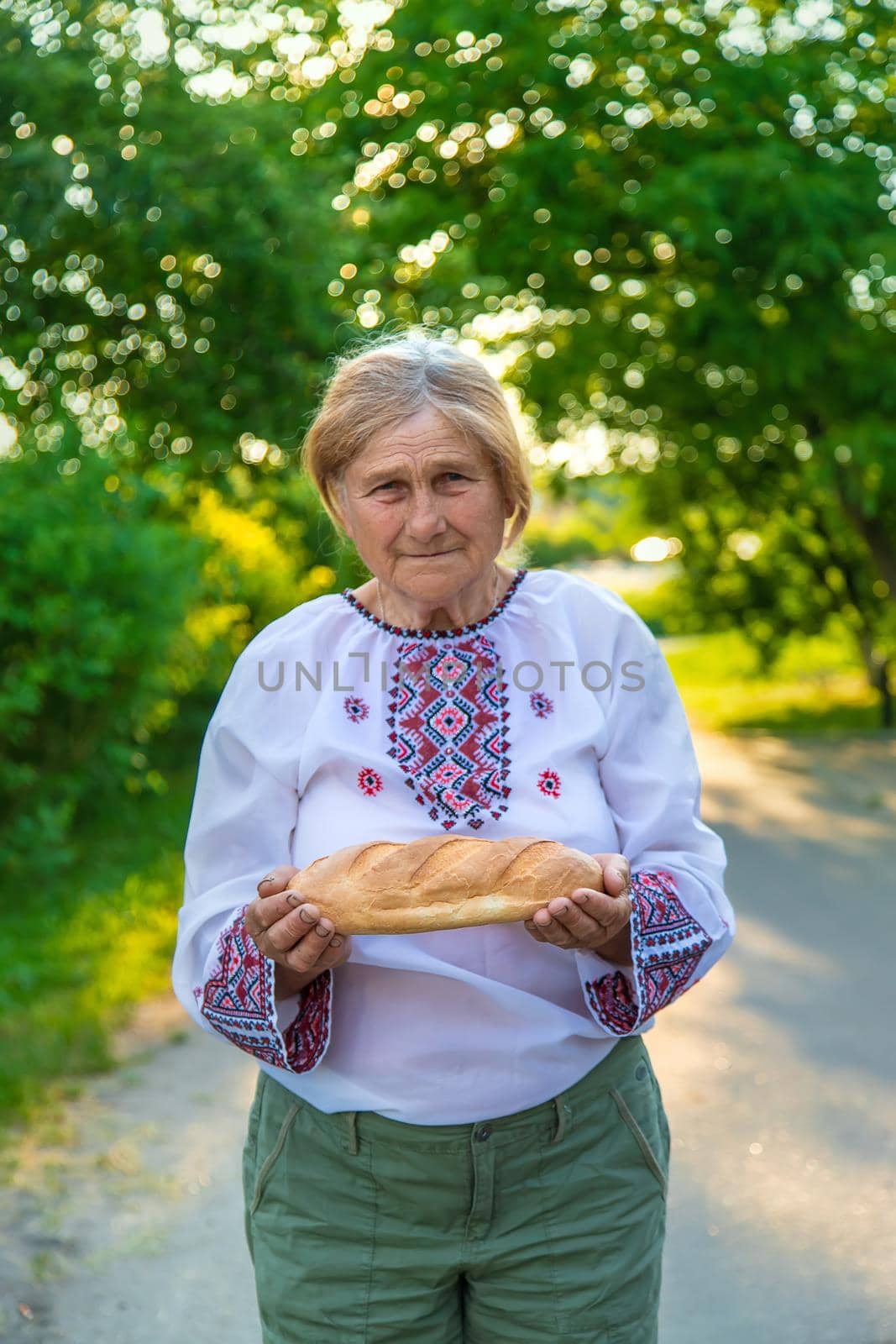 Grandmother with Ukrainian bread in her hands. Selective focus. by yanadjana