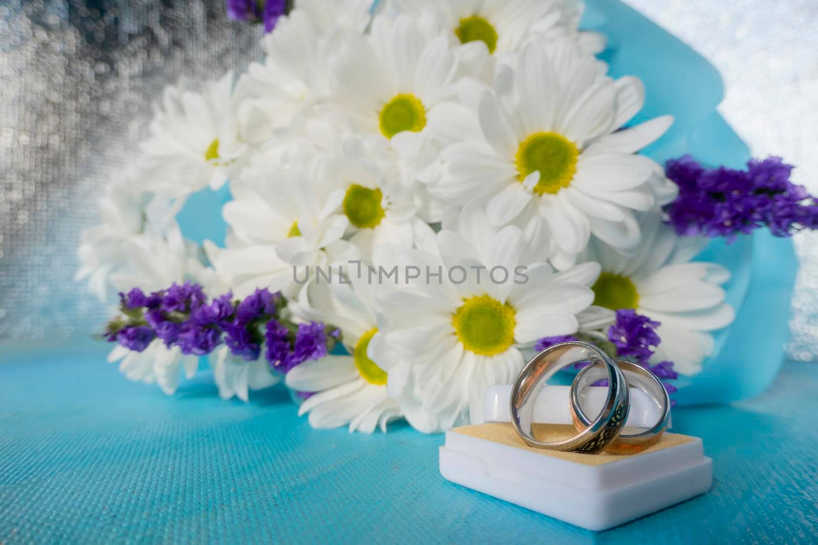 Wedding bouquet of bride. wedding card with original rings in a white box, a bouquet of white chrysanthemums or daisies and a white lace fan on a blue background