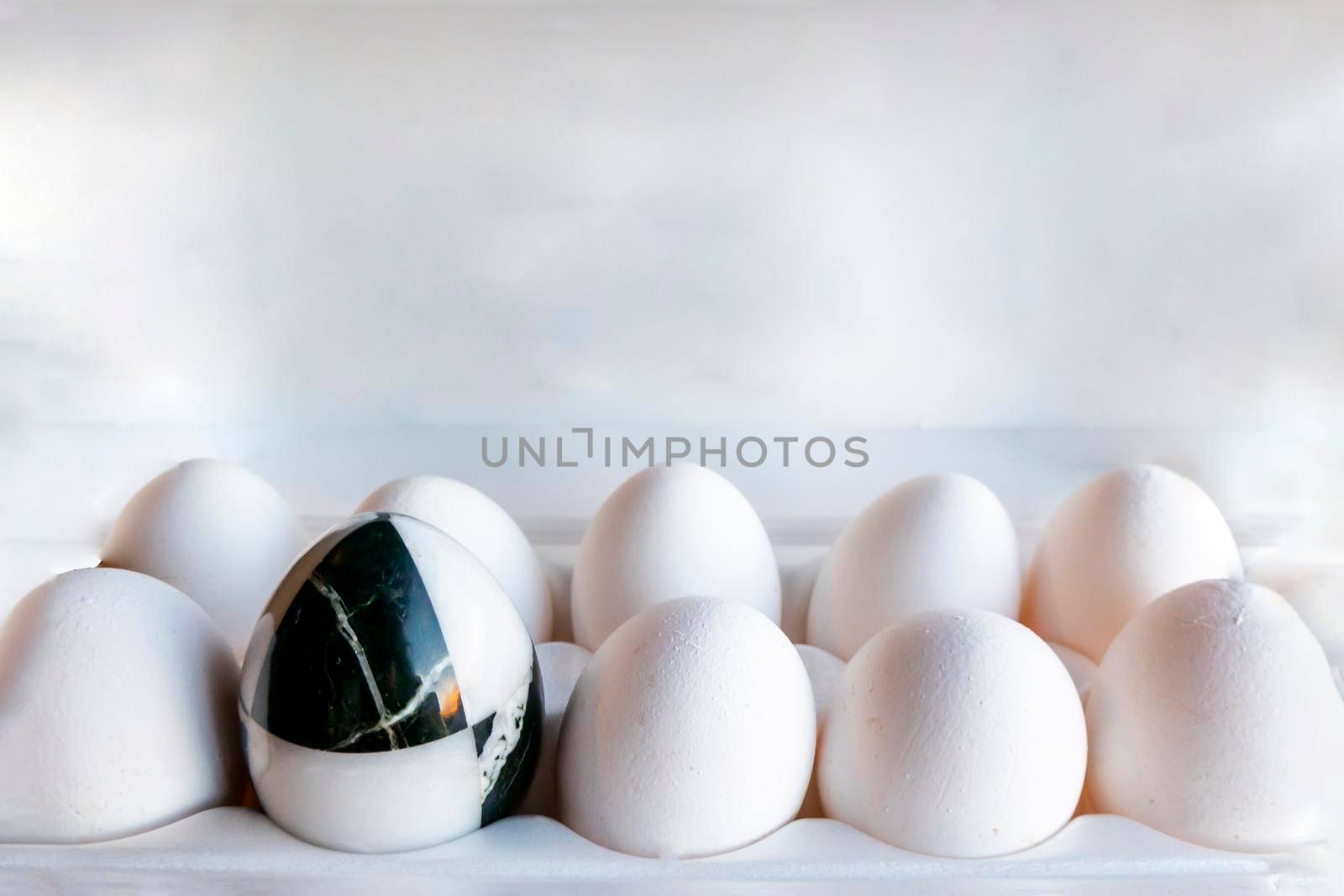 Eggs of different colors in cardboard boxes. A marble stone black-and-white egg stands in a cassette in the middle of white chicken eggs. The concept of contrast, individuality, exclusivity. concept of a damaged tooth