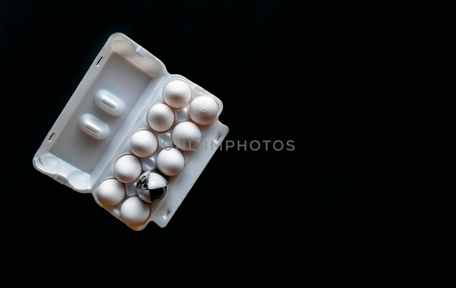 Chicken eggs in the cassette box on a black background. A marble stone black-and-white egg stands in a cassette in the middle of white chicken eggs. The concept of contrast, individuality, exclusivity. Banner on a black background with space for text