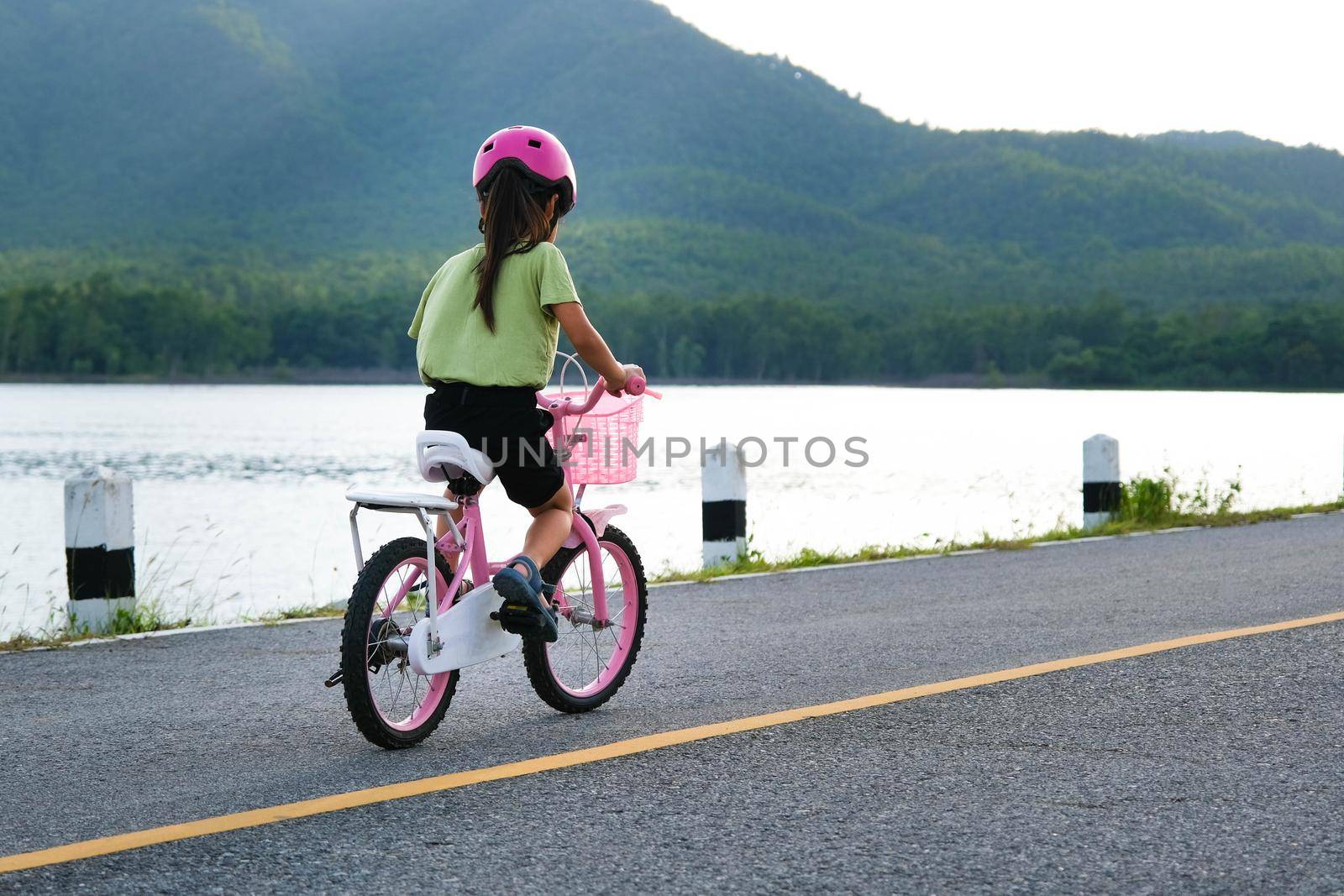 Cute little girl in a helmet riding a bicycle on an asphalt road in summer. Happy little girl riding a bicycle outdoors. Healthy Summer Activities for Kids by TEERASAK