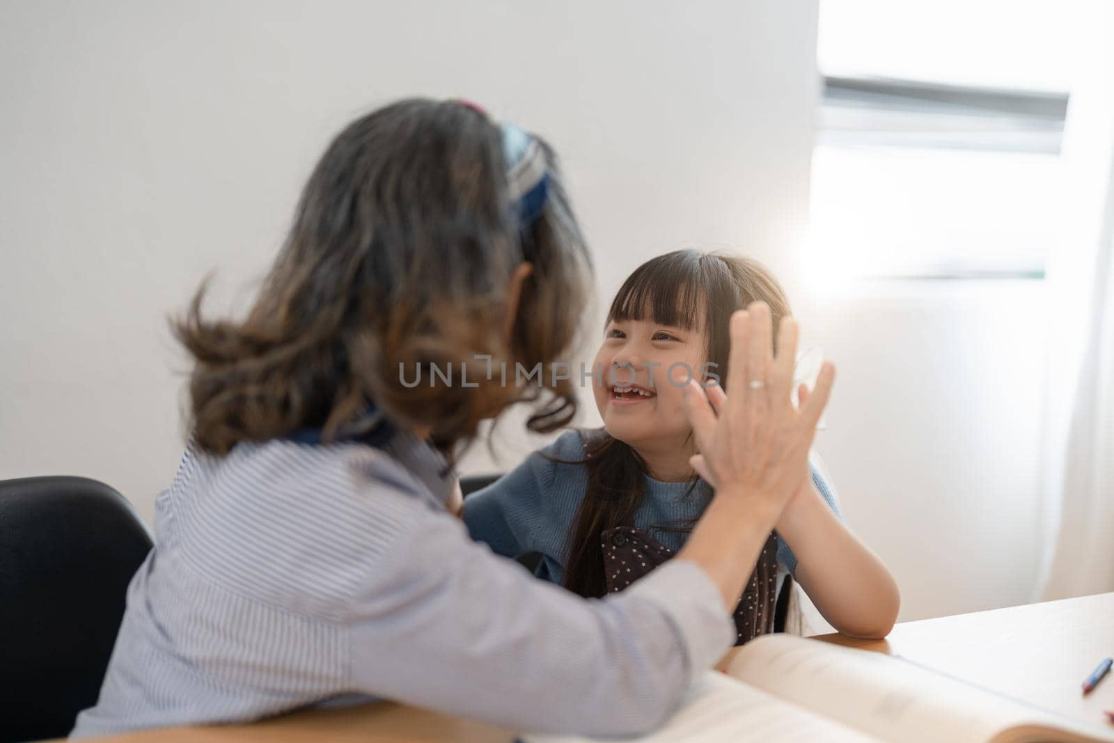 Little granddaughter and happy grandmother giving high five having fun playing together sitting on sofa, smiling grandma granny and preschool grandchild laughing celebrating good relations at home.