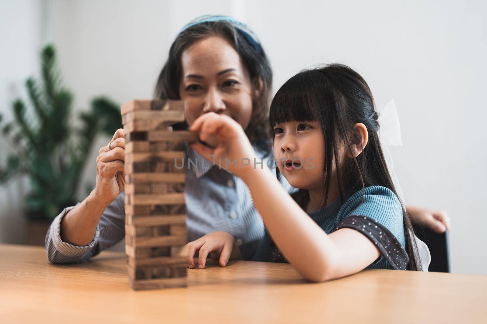 Happy moments of Asian grandmother with her granddaughter playing jenga constructor. Leisure activities for children at home