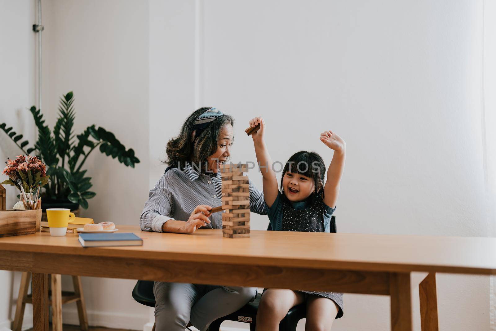 Happy exciting moments of Asian grandmother with her granddaughter playing jenga constructor. Leisure activities for children at home