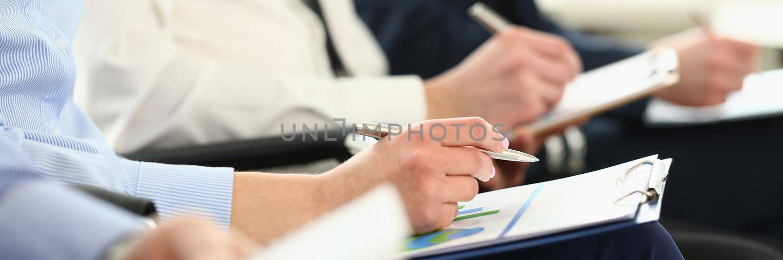 Group of business people sitting in audience with documents with charts closeup. Company meeting concept