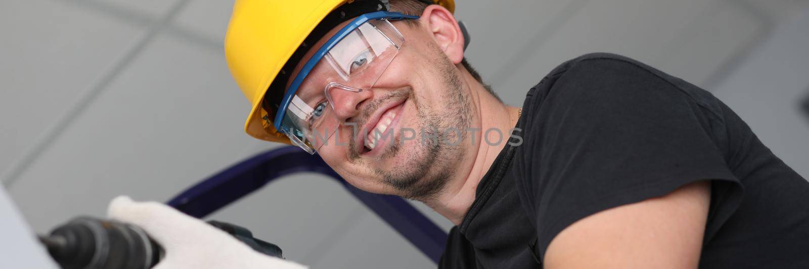 Smiling builder in helmet drilling wall in house. Apartment renovation concept