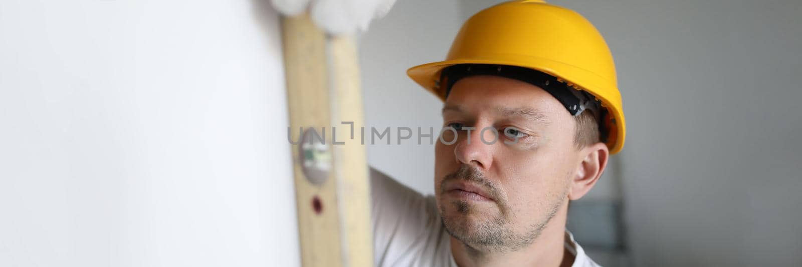 Man in helmet measuring wall using building level in apartment. Repair and construction of houses concept