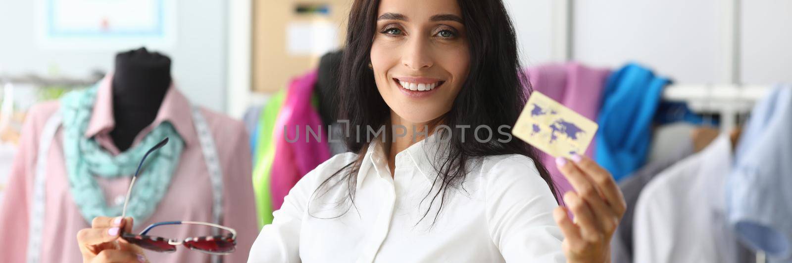 Smiling woman holding plastic credit card in clothing salon. Shopping and fashion concept