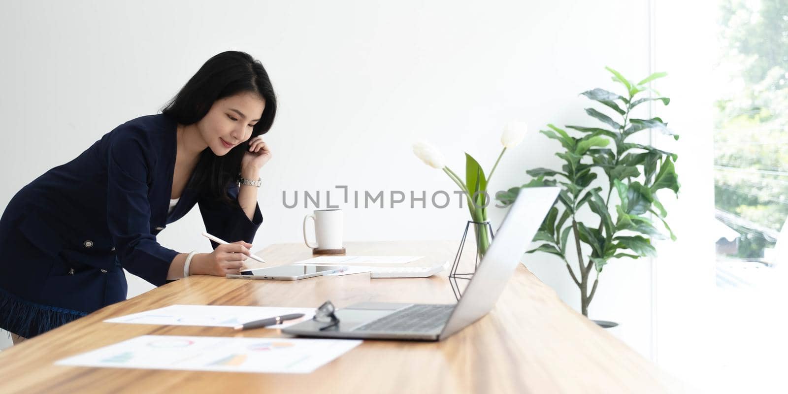 Beautiful Asian businesswoman analyzes charts using laptop calculator at the office. by wichayada