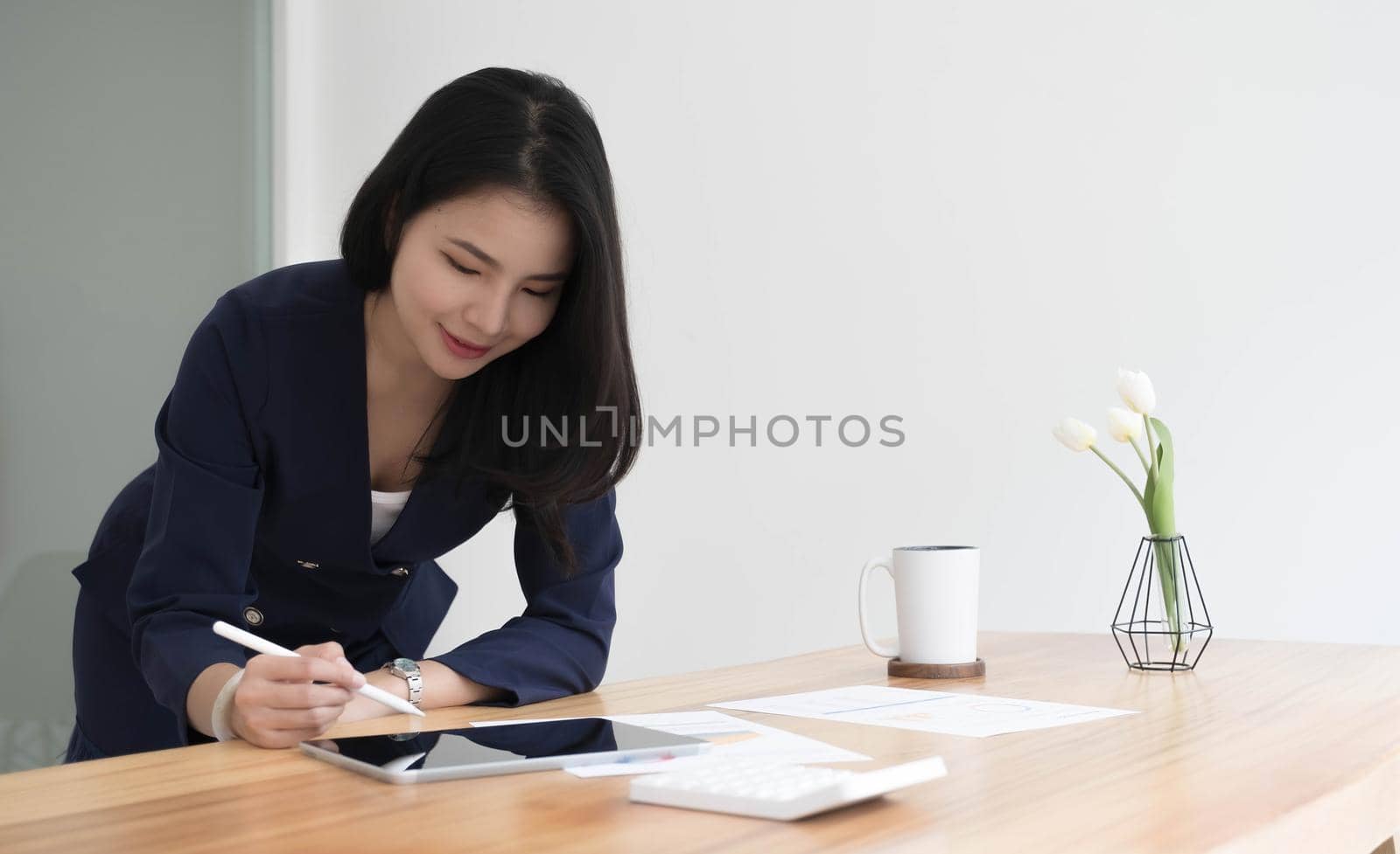 Beautiful Asian businesswoman analyzes charts using laptop calculator at the office..