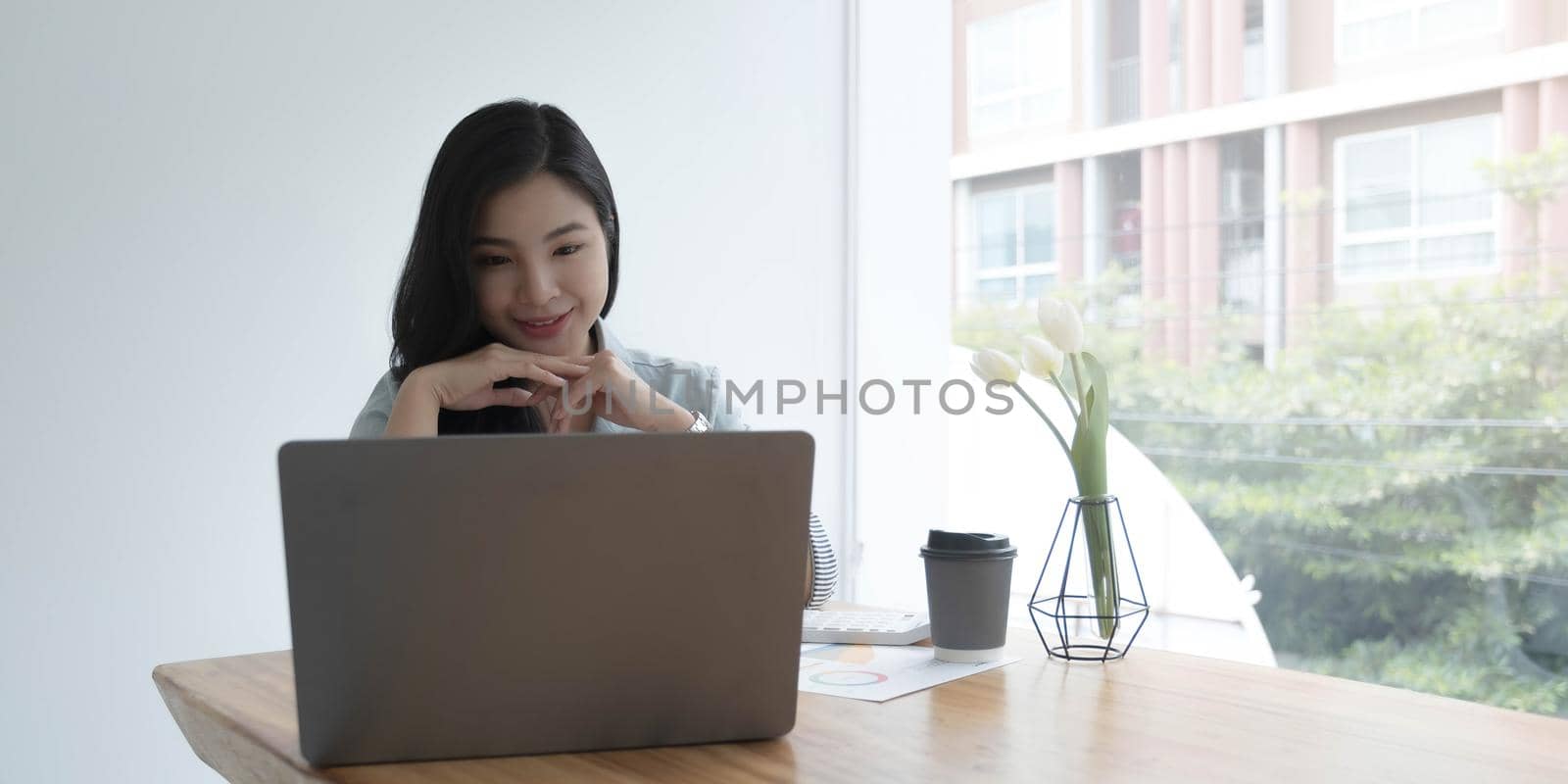 Happy young asian businesswoman sitting on her workplace in the office. Young woman working at laptop in the office..