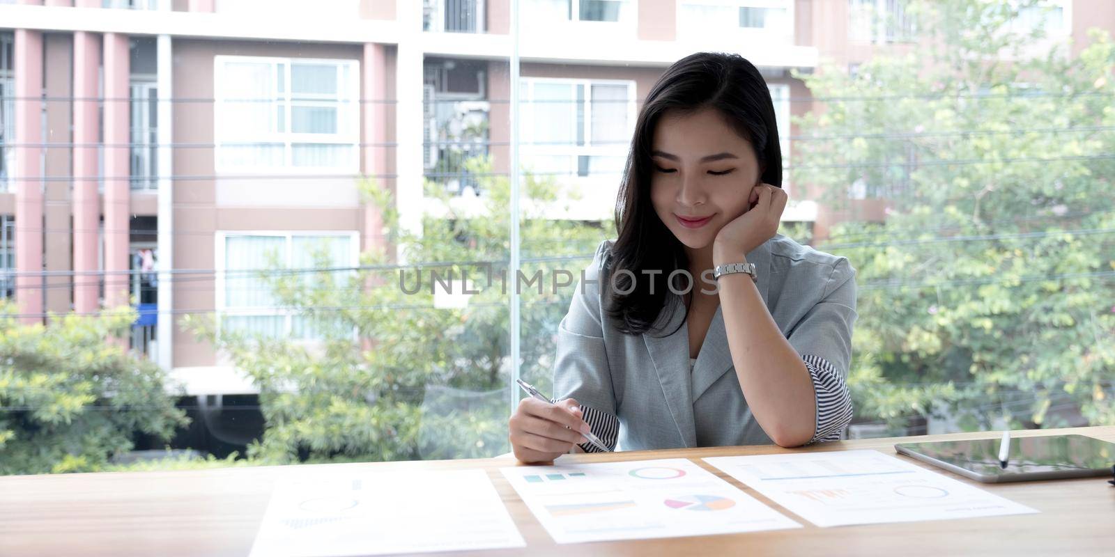 Beautiful Asian businesswoman analyzes charts using laptop calculator at the office. by wichayada