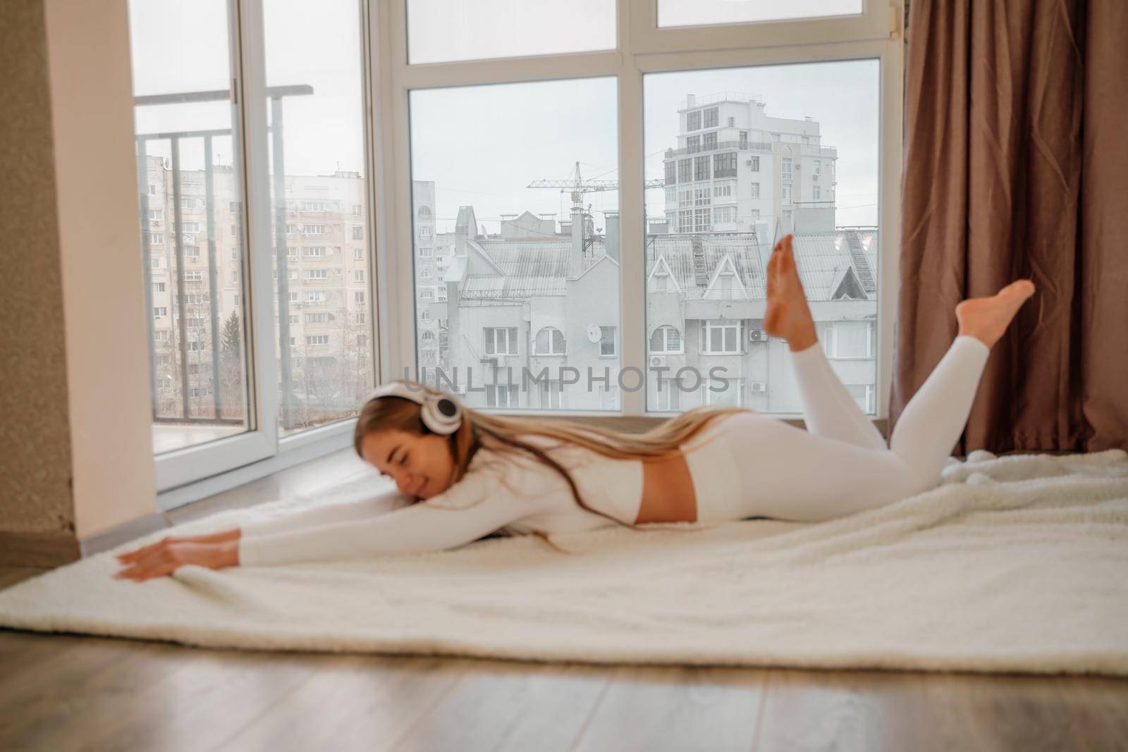 Side view portrait of relaxed woman listening to music with headphones lying on carpet at home. She is dressed in a white tracksuit