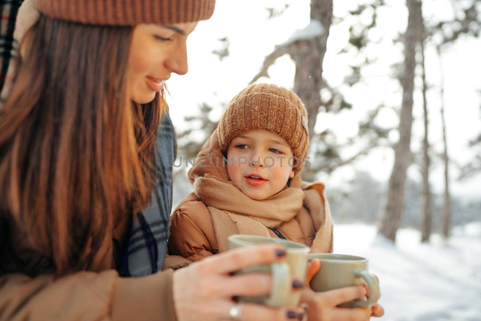 Young woman with a son in winter forest on a picnic drink hot tea, close up