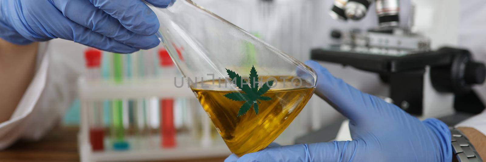 Chemist in gloves holding flask with marijuana oil in laboratory closeup. Illegal production of narcotic drugs concept