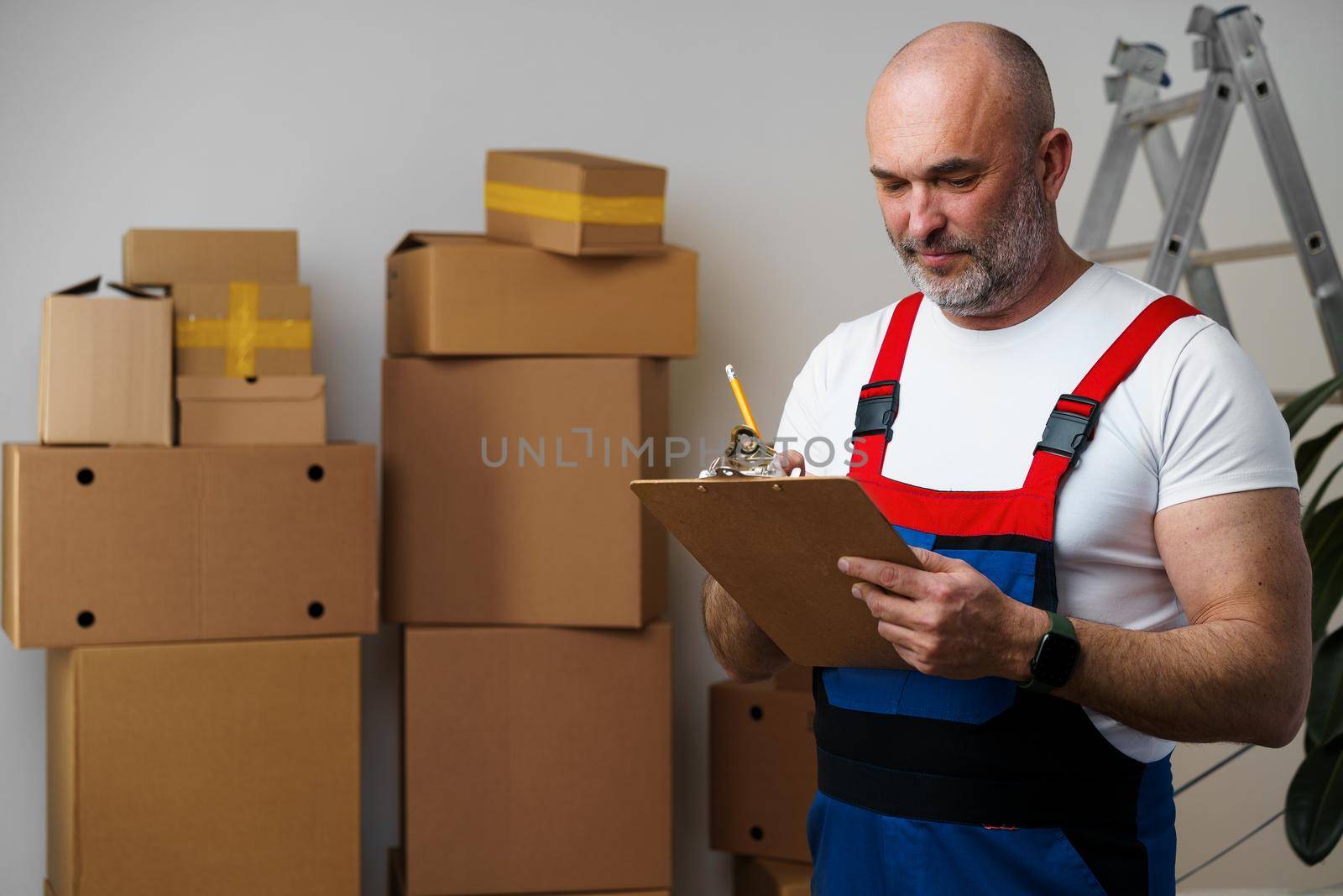 Middle-aged man mover in uniform making notes on clipboard, close up