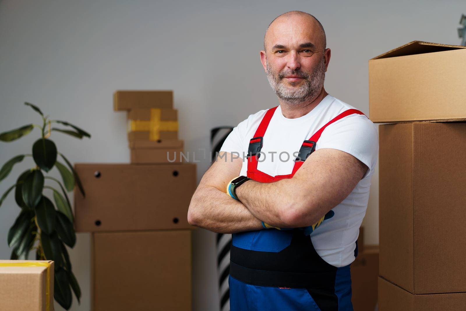 Portrait of a middle-aged man mover in uniform standing against stacked boxes, close up