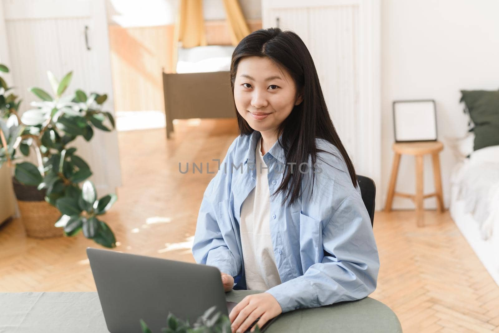 Young Asian woman working on a laptop at home and looking at the camera. Freelance business concept. Web banner.