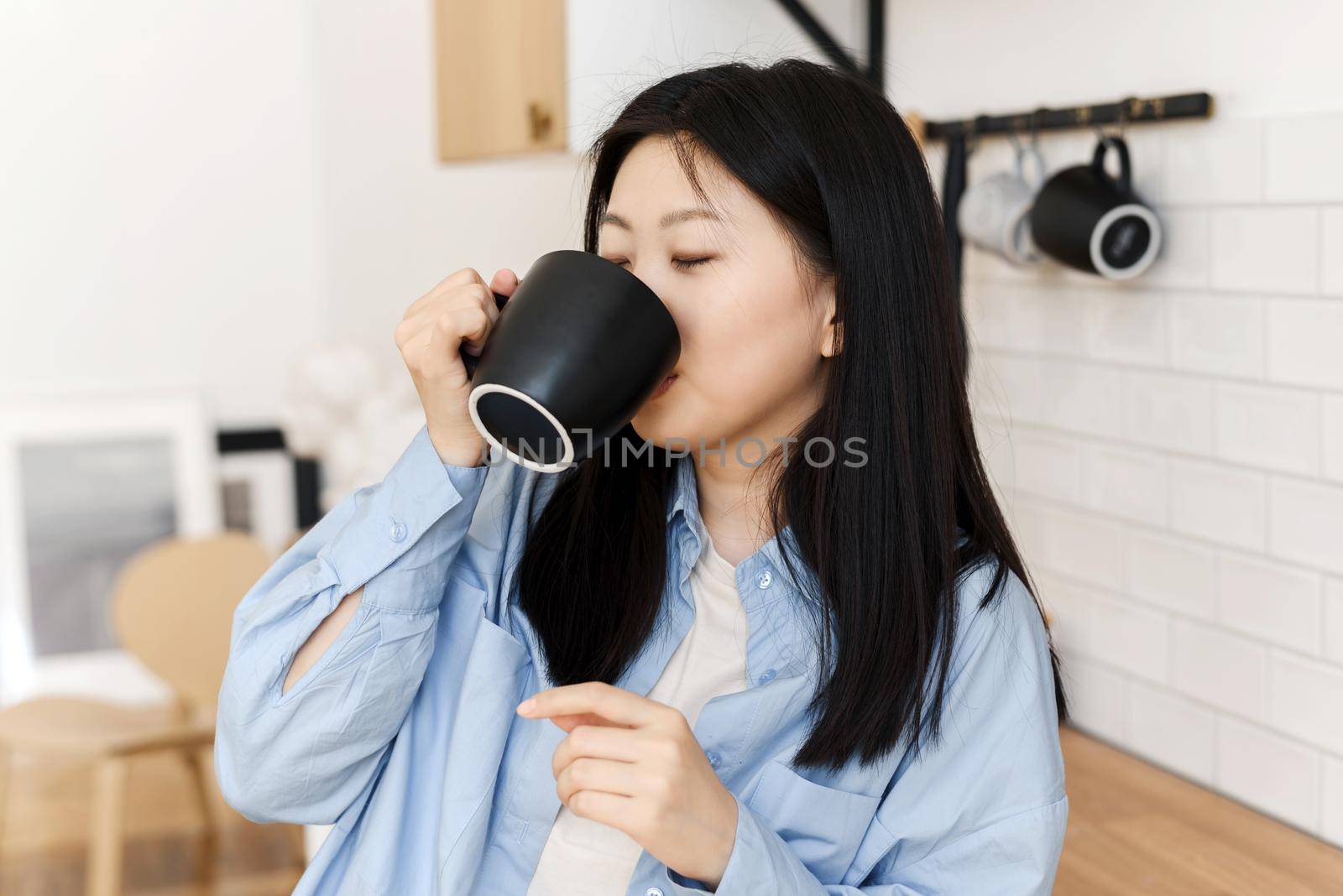 A charming Korean woman in the kitchen, holding a cup of coffee or tea