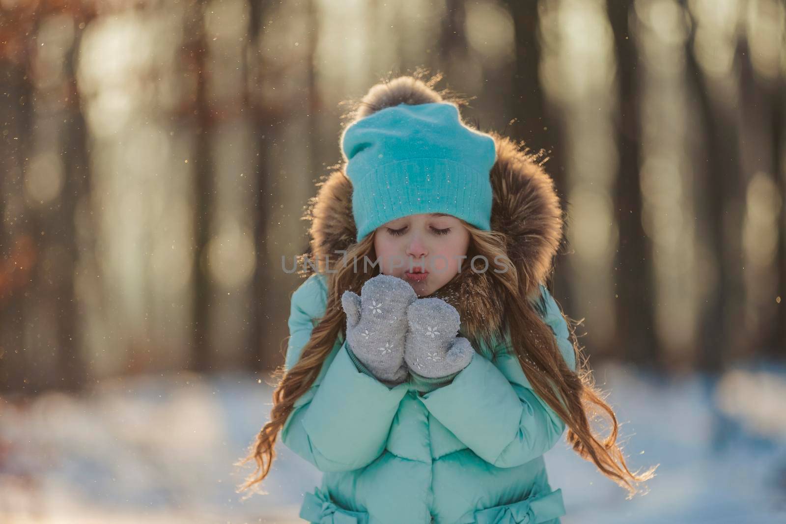 little girl blows on the snow that is on her mittens