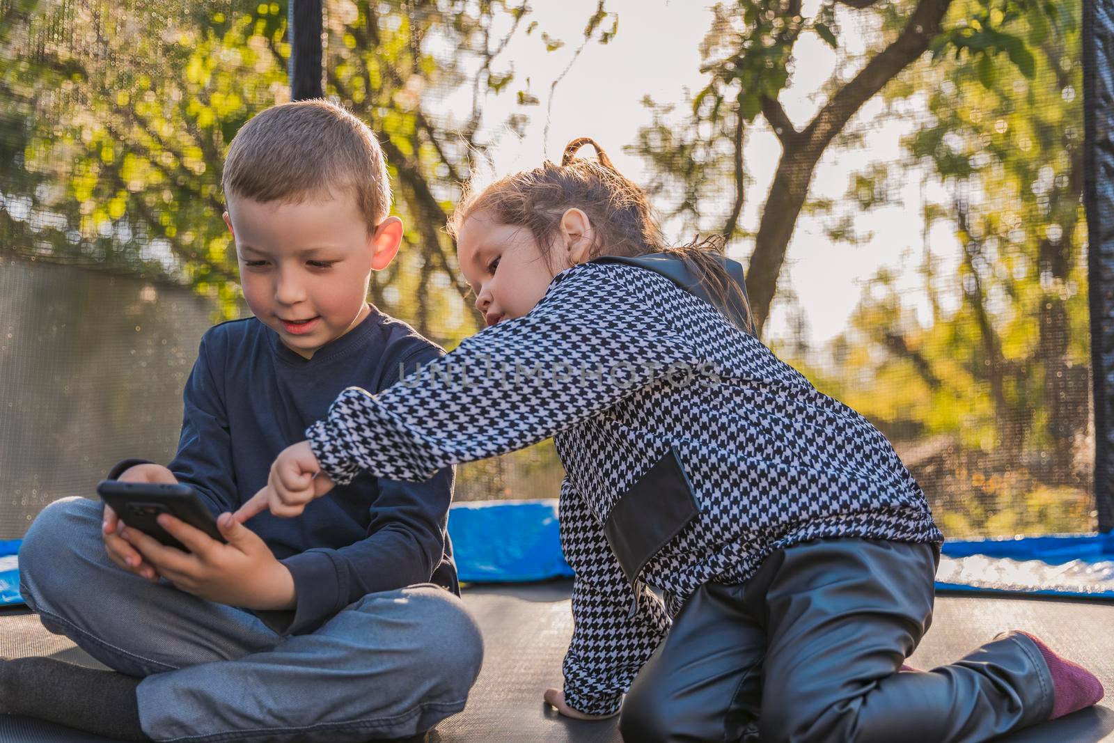 children sit on a trampoline and look at the phone