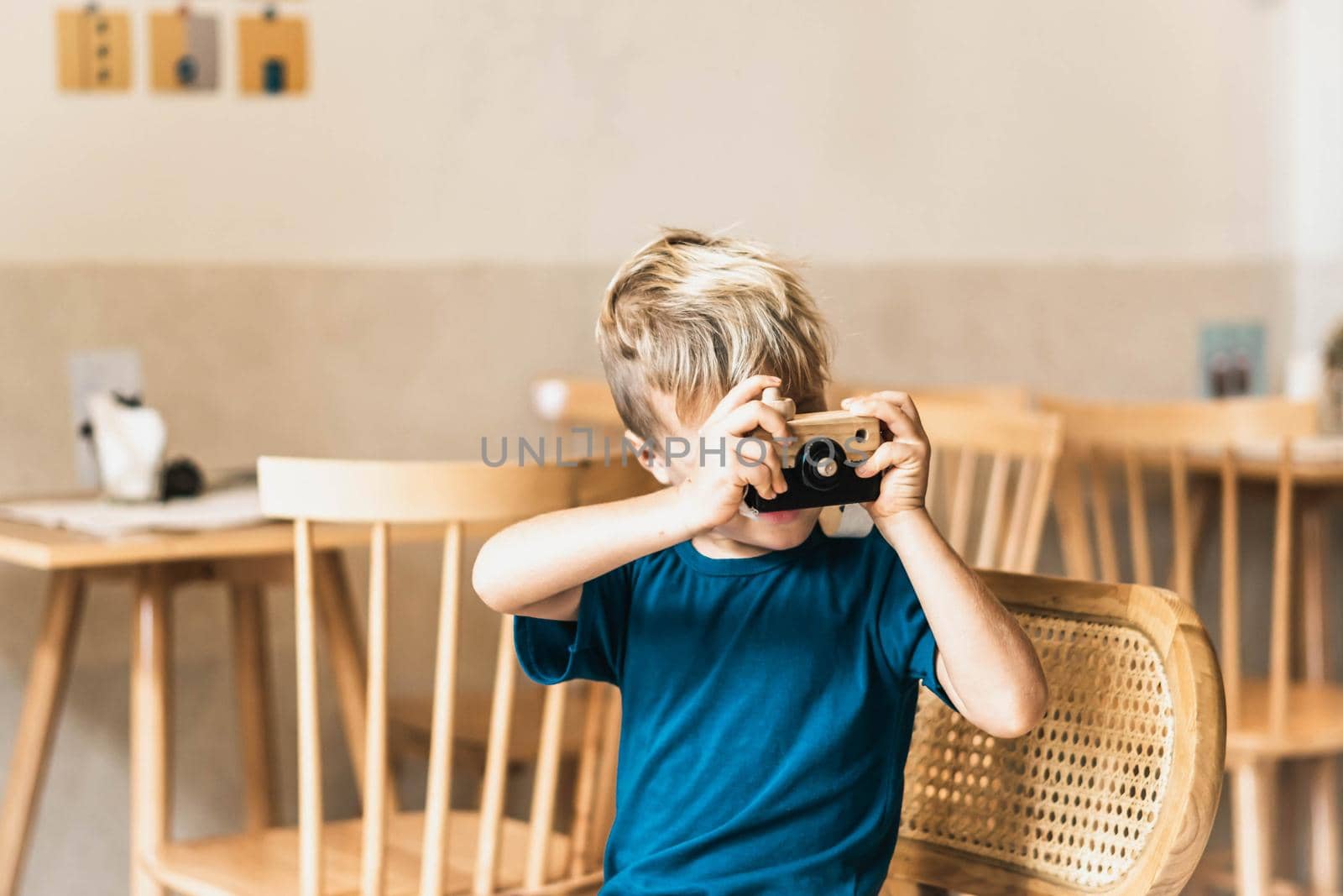 Cute happy smile little boy play handmade wooden photo camera, hold toy in hands. Artistic craft activities. Preschool children development skills future creative profession. Modern cozy class room.