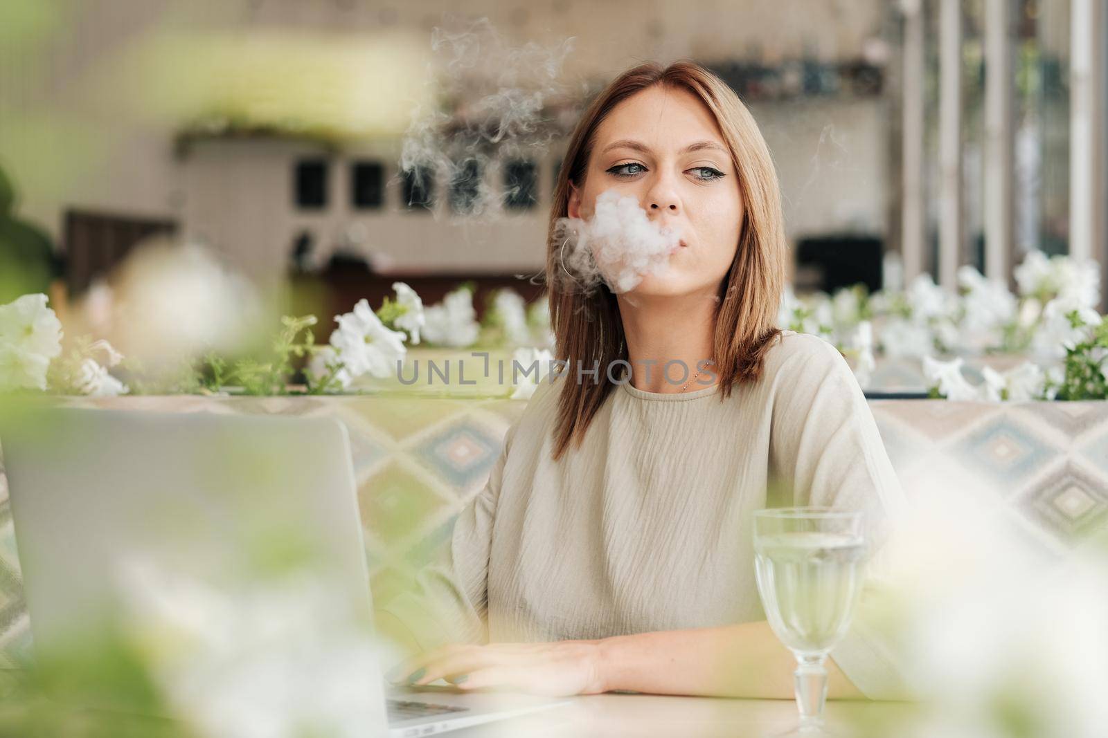 Young Woman Smoking Electronic Cigarette in Restaurant While Working on Laptop