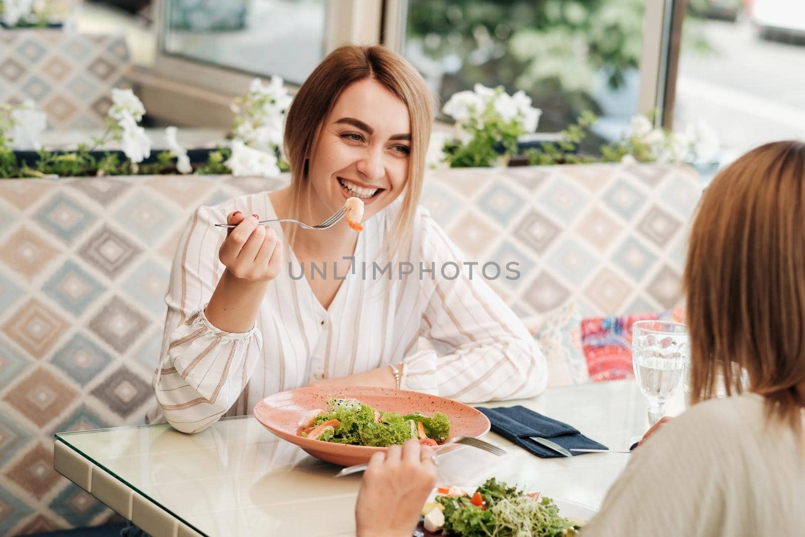 Cheerful Young Woman Having Lunch with Her Female Friend, Eating Salad with Shrimp in Restaurant