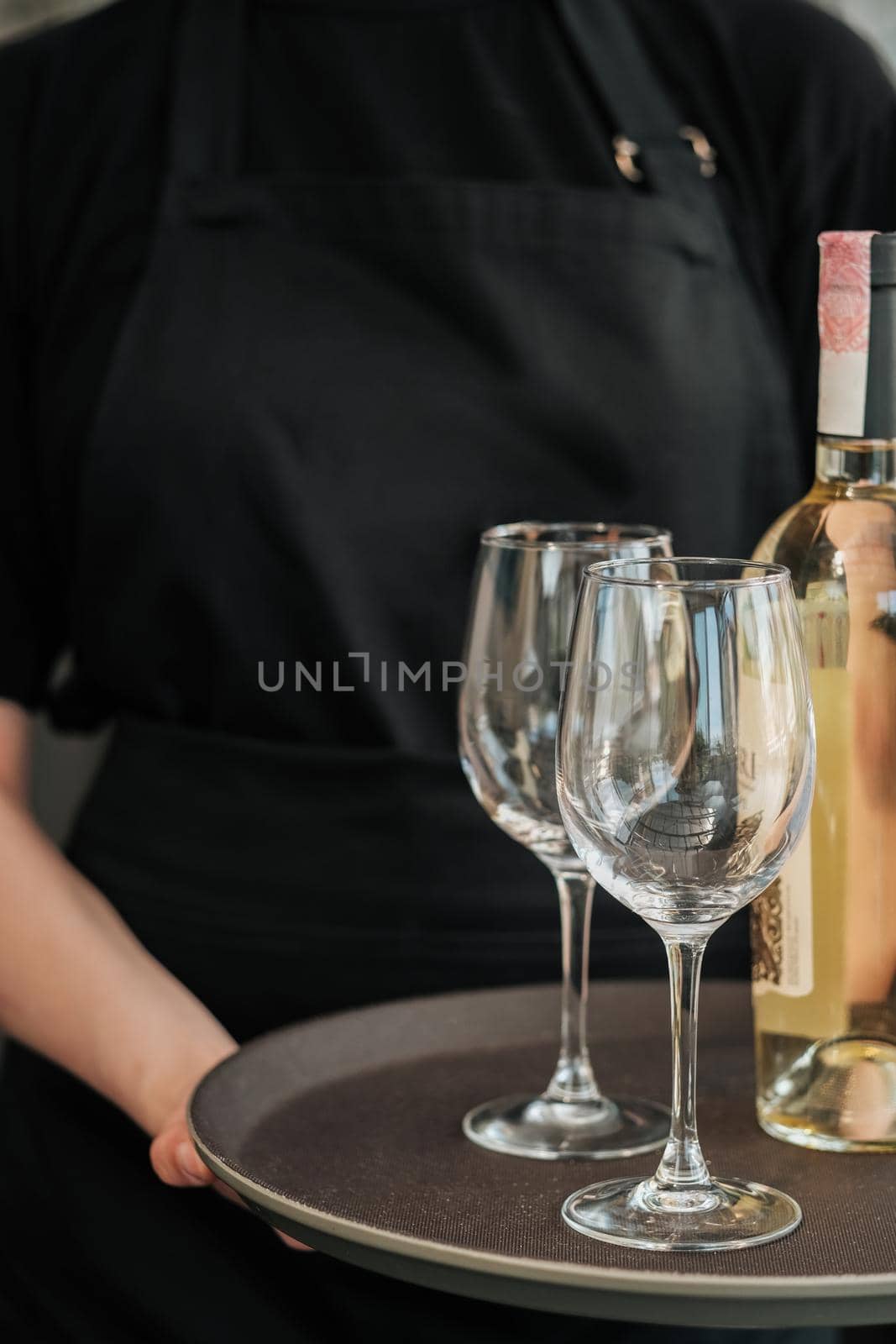 Close Up of Female Waiter Holding Bottle of White Wine and Glass on Tray in Restaurant