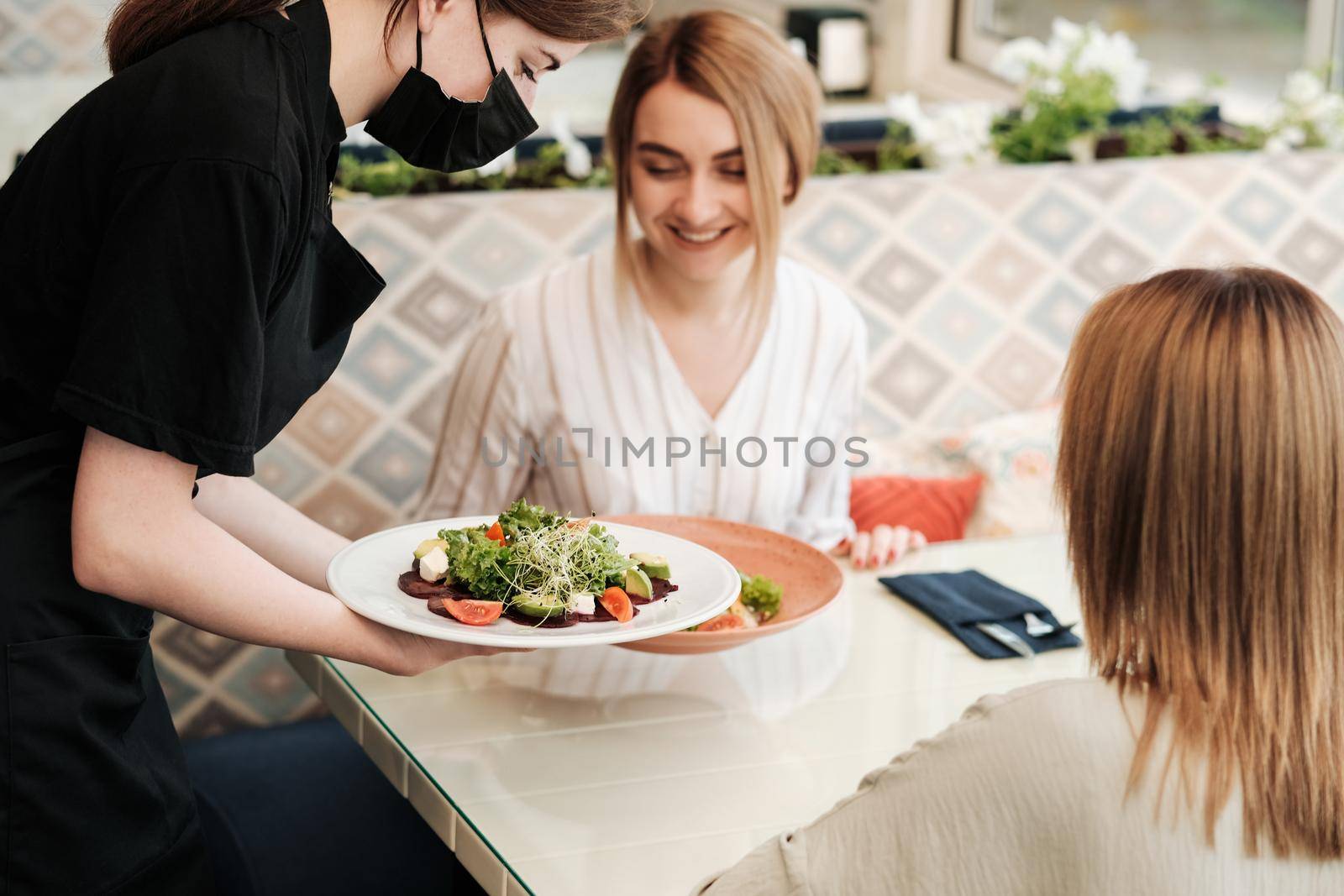 Female Waiter Bringing Order for Two Young Women in Restaurant