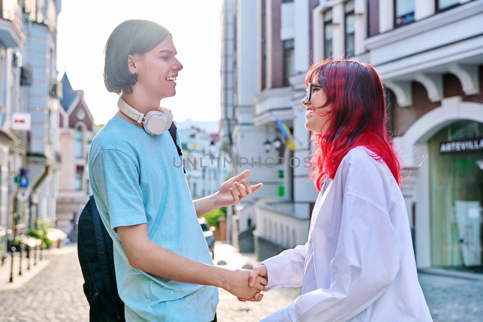 Meeting, shaking hands teenage male and female friends on the city street by VH-studio