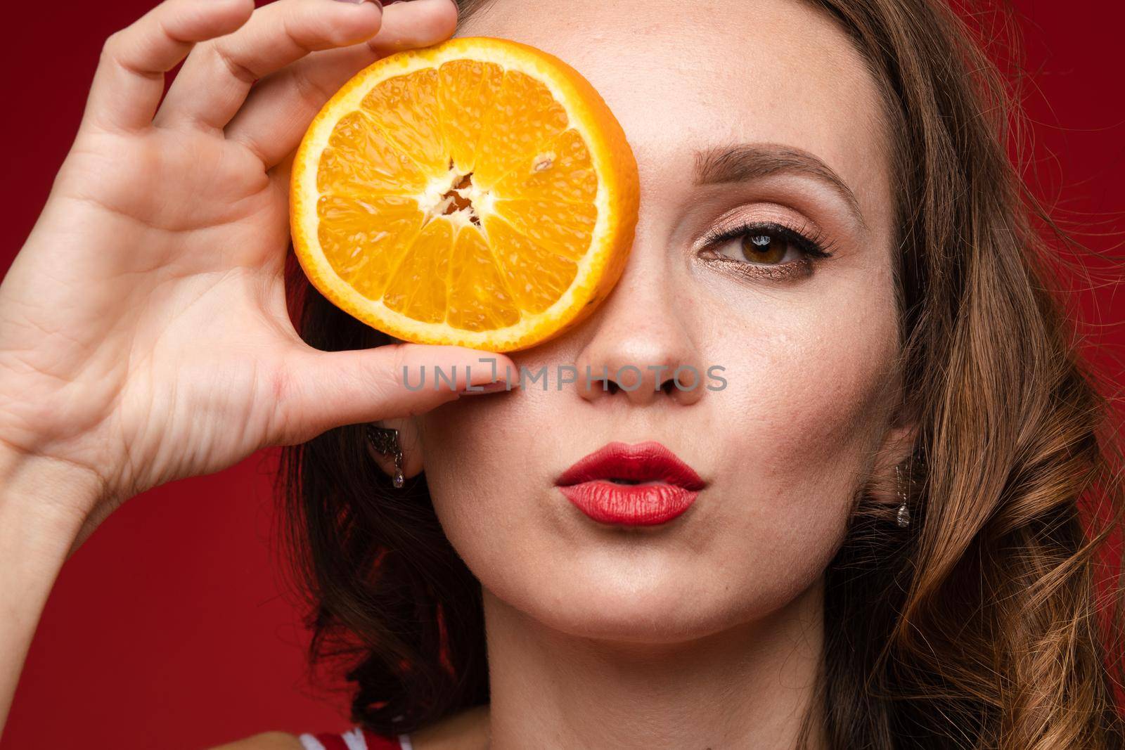 Beautiful woman in a red swimsuit with bright makeup and red lips with orange slices, summer, brightness, joy.